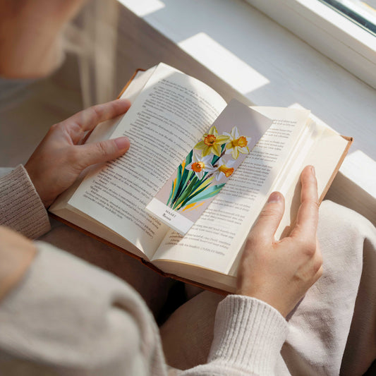 vrouw die boek leest, op de pagina van het opengeslagen boek ligt een boekenlegger . geboorte bloem boekenlegger voor de maand maart, met  kunstzinnige illustratie van Narcissen