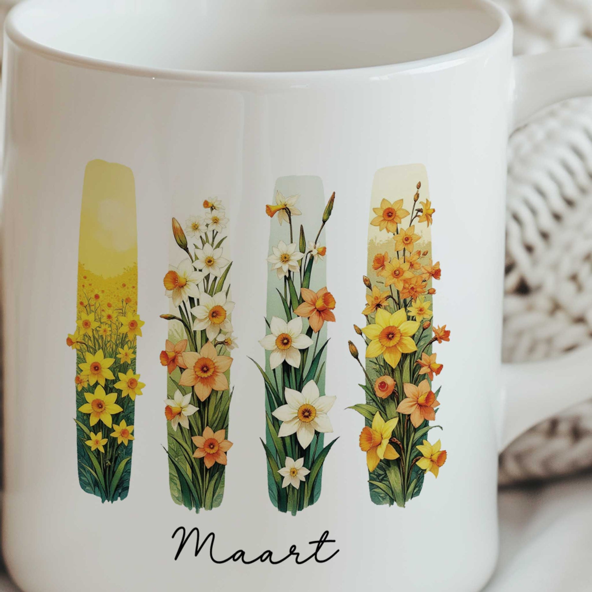 Close-up van een witte mok met brush effect van gele en witte narcissen, de geboortebloem van maart, waarbij het bloemenontwerp duidelijk zichtbaar is.
