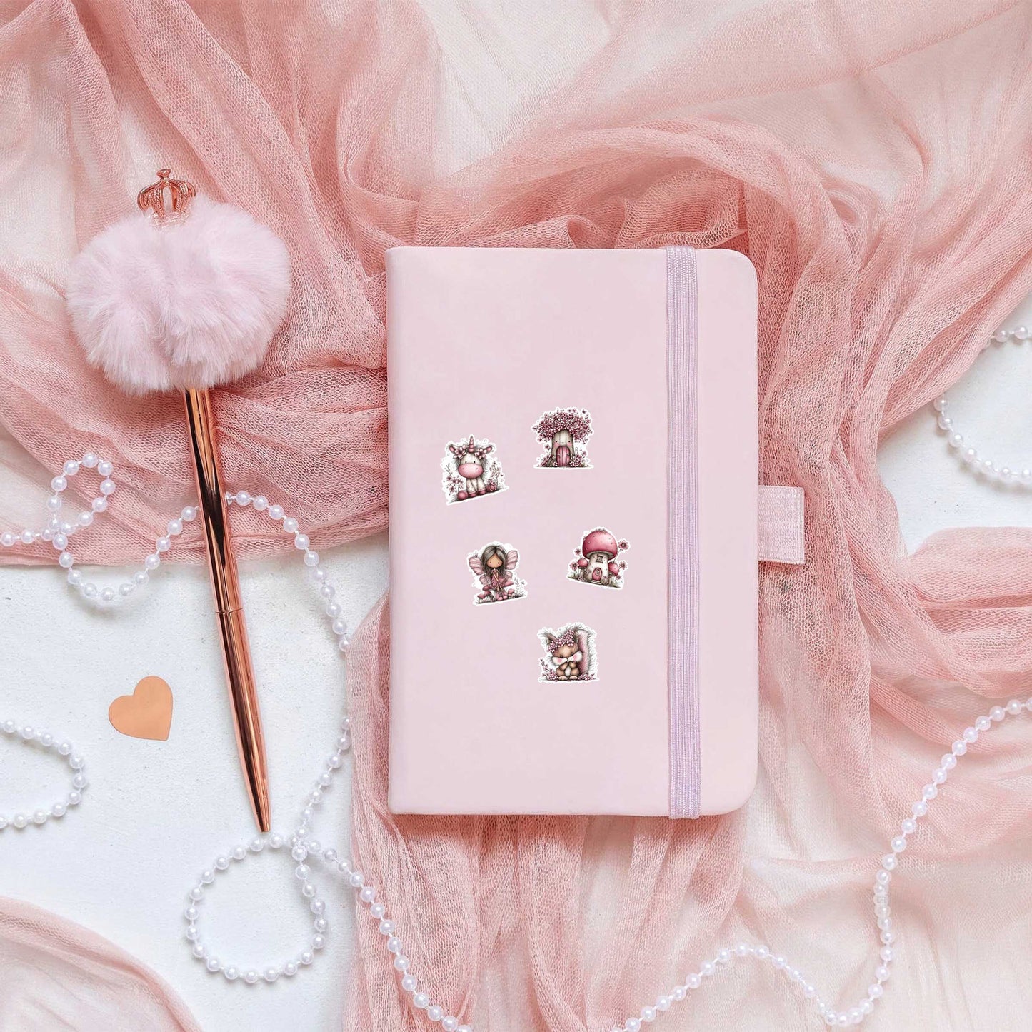 Roze notitieboek versierd met vijf stickers uit het stickervel Magisch Sprookjesbos, naast een roze pen met pluim, parelsnoer en roze tule.