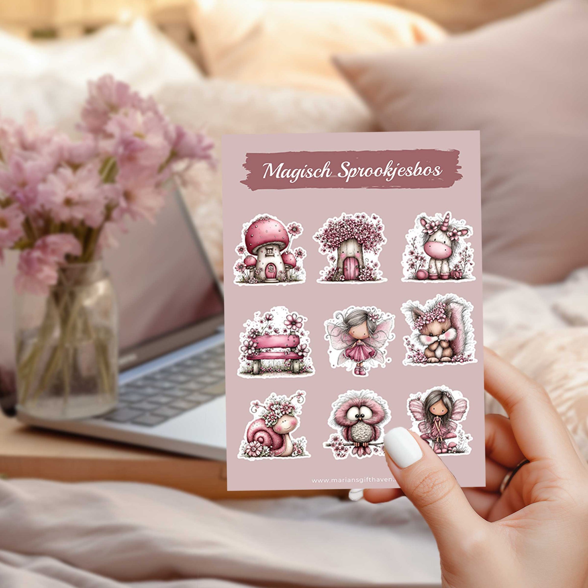 Hand houdt het stickervel Magisch Sprookjesbos vast boven een bed met op de achtergrond een laptop en een vaas met roze bloemen.