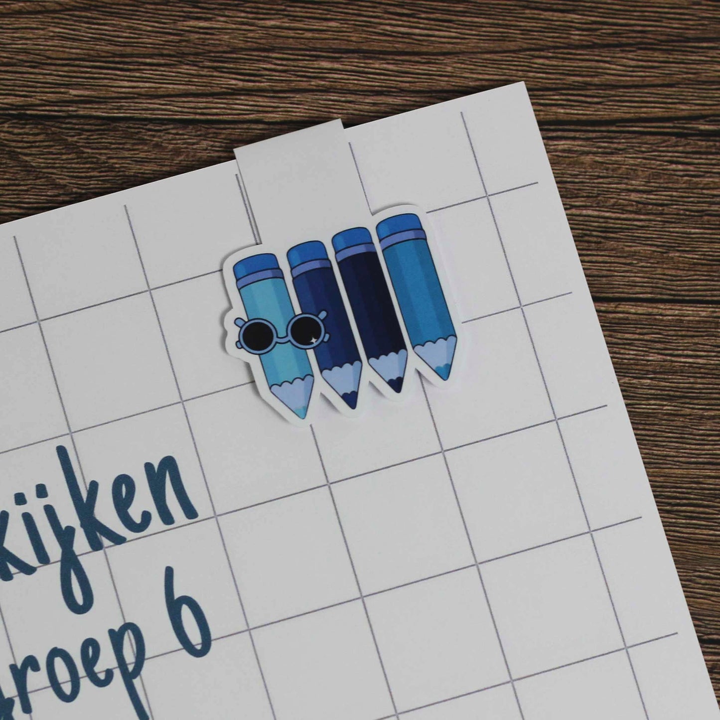 Magnetische boekenlegger met blauwe potloden geplaatst op een schrift met ruitjespagina als gebruiksvoorbeeld