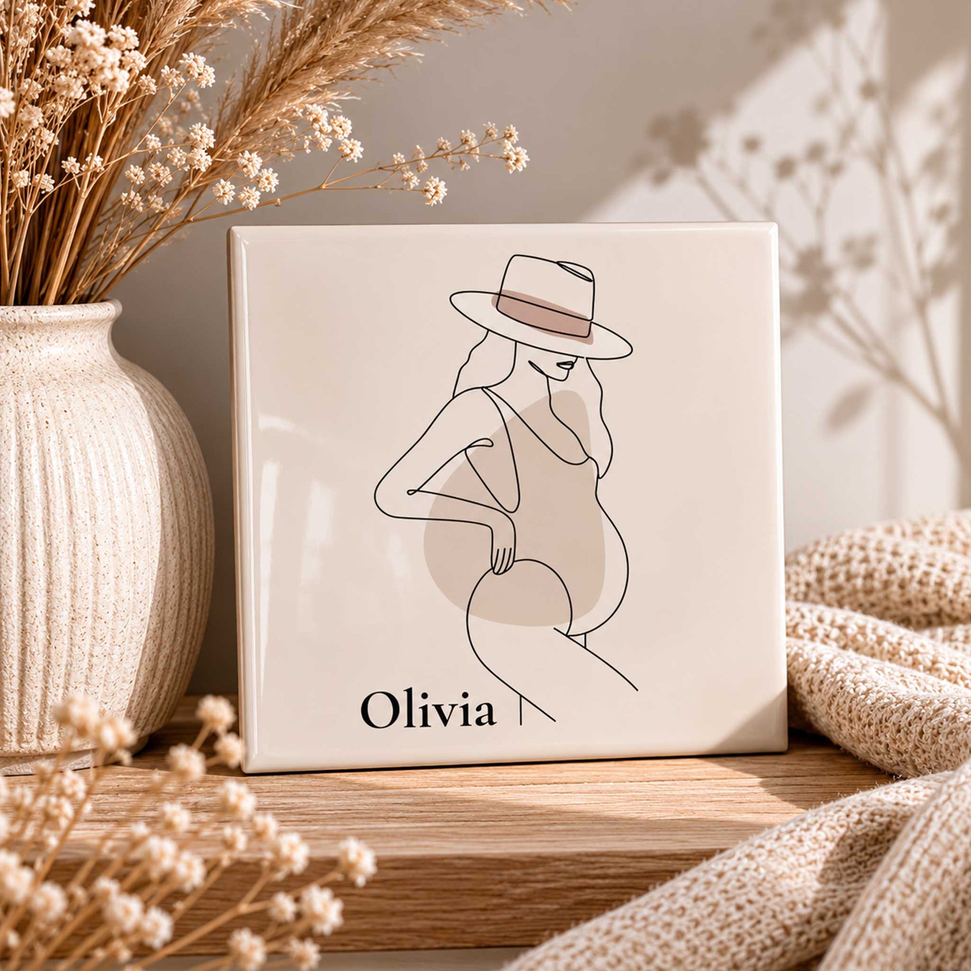 Keramisch zwangerschap tegeltje met naam Olivia op houten plankje tussen droogbloemen en beige woondecoratie