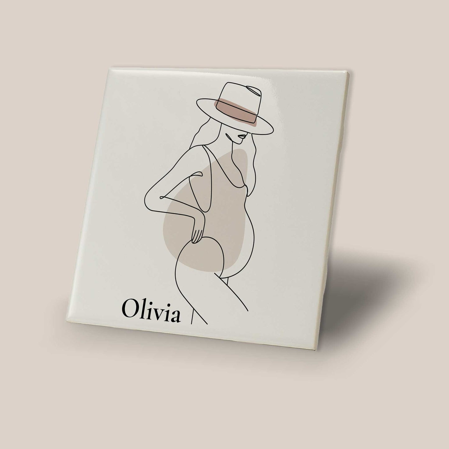 Schuin gefotografeerd keramisch zwangerschap tegeltje met minimalistische illustratie van zwangere vrouw en naam Olivia