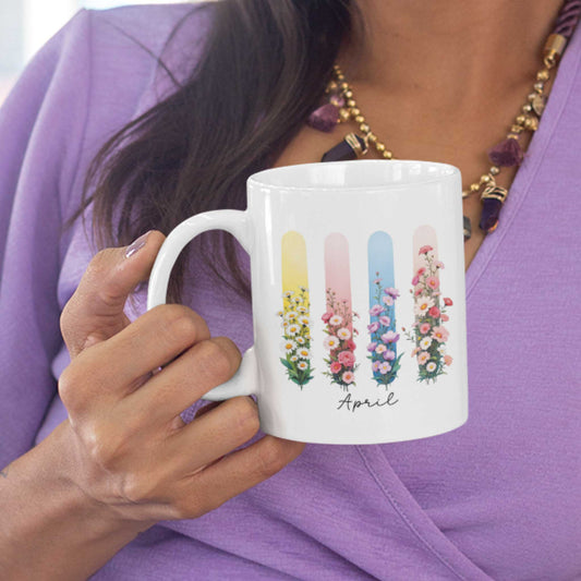 Vrouw in lila blouse houdt een mok vast met madeliefjes en lathyrus in pastel brushstijlen, met ‘April’ in sierlijke script.