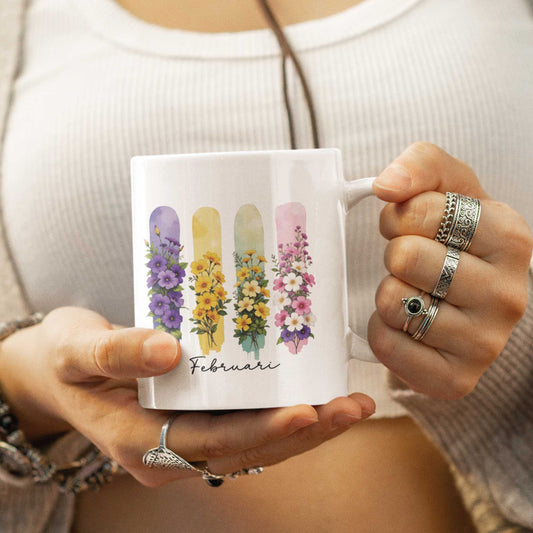 Vrouw in witte top houdt een mok vast met kleurrijke bloemenillustraties en het woord 'Februari' in sierlijk lettertype.