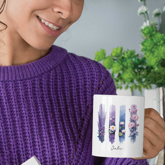 Vrouw in paarse trui houdt een mok vast met ridderspoor en waterlelie in aquarel brushstijl, met het woord ‘Juli’ in sierlijke script.