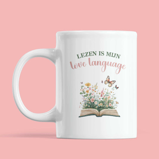 Witte mok met illustratie van open boek, bloemen en vlinders en de tekst Lezen is mijn love language op roze achtergrond