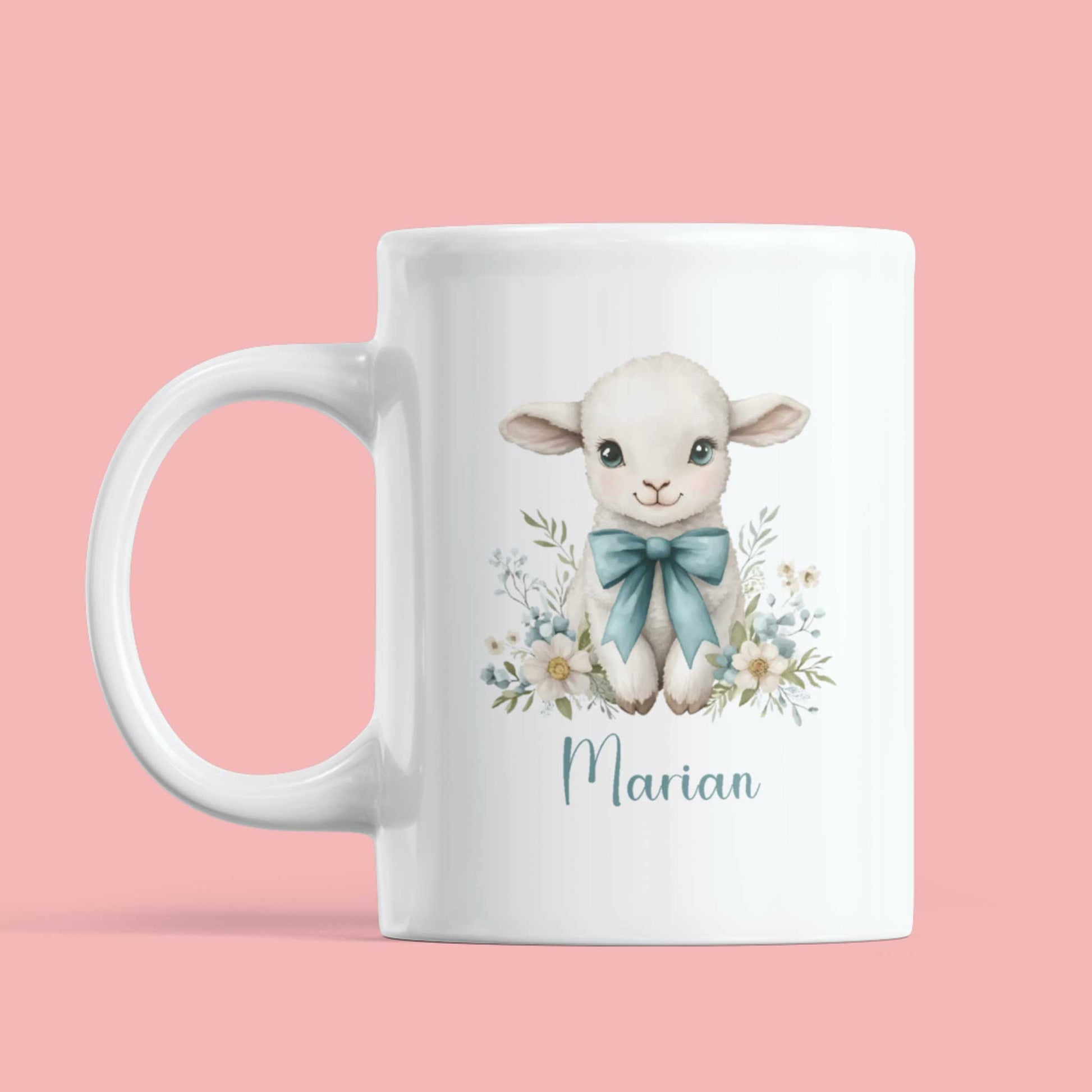 Witte mok met een aquarelillustratie van een wit lammetje met grote blauwe strik en bloemenkrans onderaan, met de naam Marian in sierlijk blauw schrift op een effen roze achtergrond.