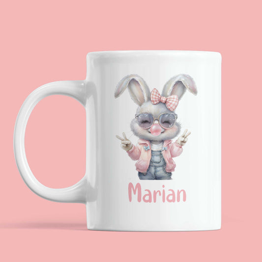 Gepersonaliseerde witte mok met cool meisjeskonijn in roze jasje, zonnebril en naam Marian in roze letters op roze achtergrond.