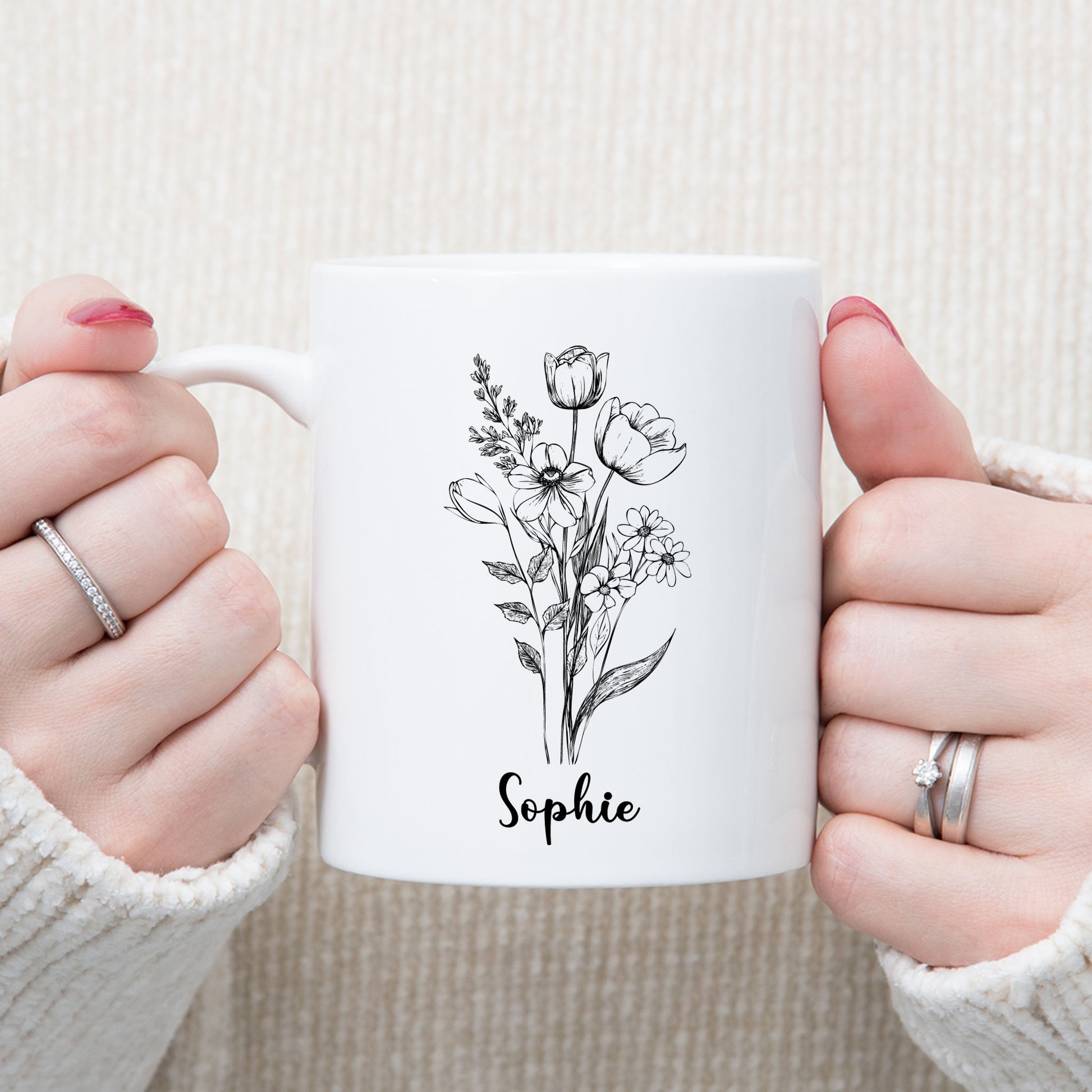 Sfeerfoto van een witte mok met een zwarte bloemenschets en de naam Sophie die met twee handen wordt vastgehouden.