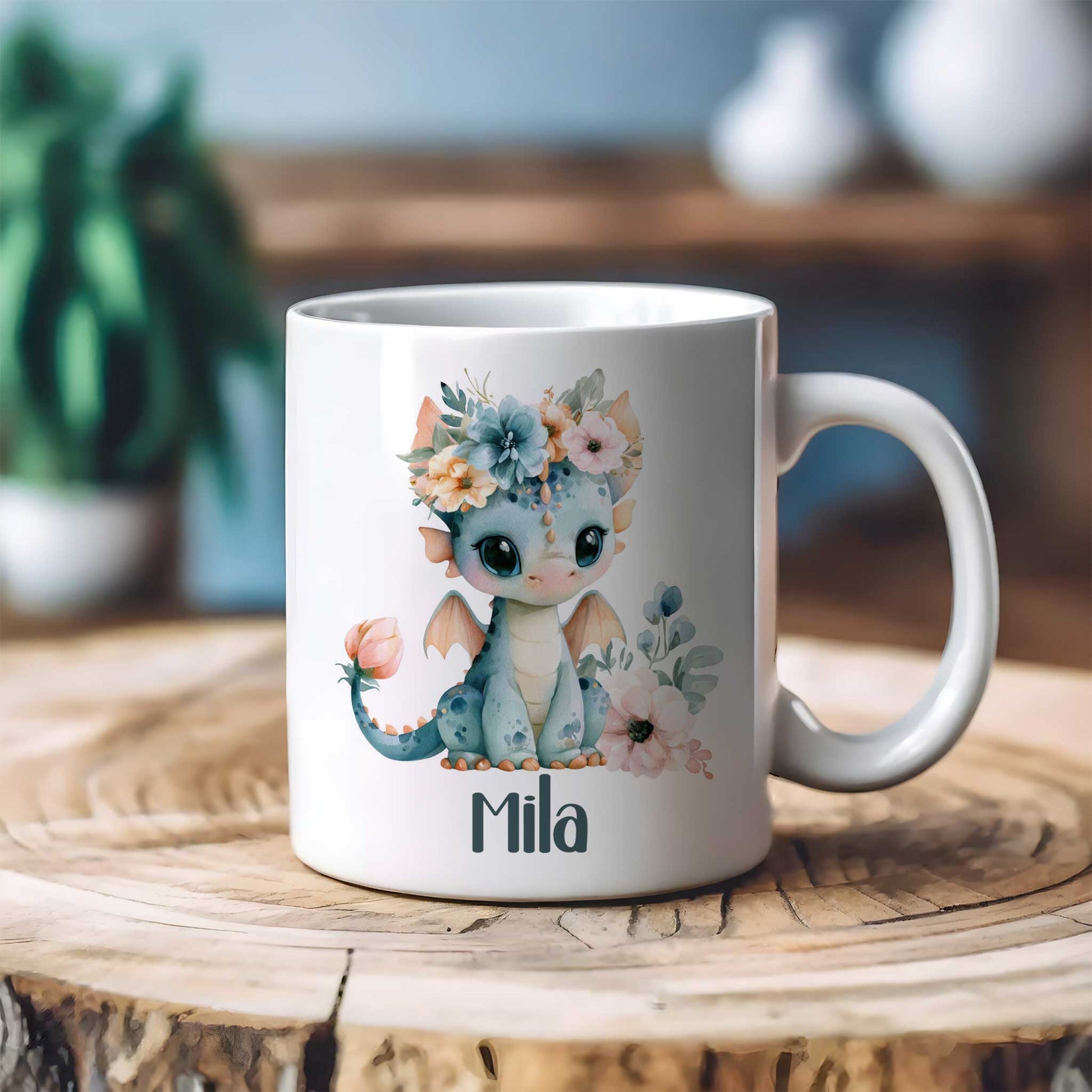 Witte mok met een blauw draakje met bloemenkroon en naam Mila op een houten tafel met een onscherpe woonkamer op de achtergrond.