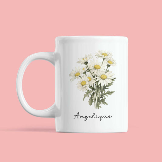 Witte gepersonaliseerde mok met boeket madeliefjes en naam Angelique, voor roze achtergrond.
