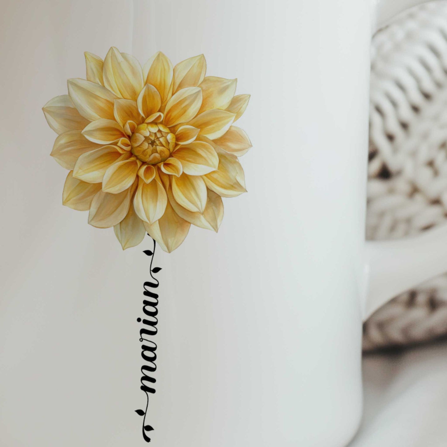 Close-up van een witte mok met een gedetailleerde gele dahlia en een gepersonaliseerde naam die als bloemsteel onder de bloem is verwerkt.