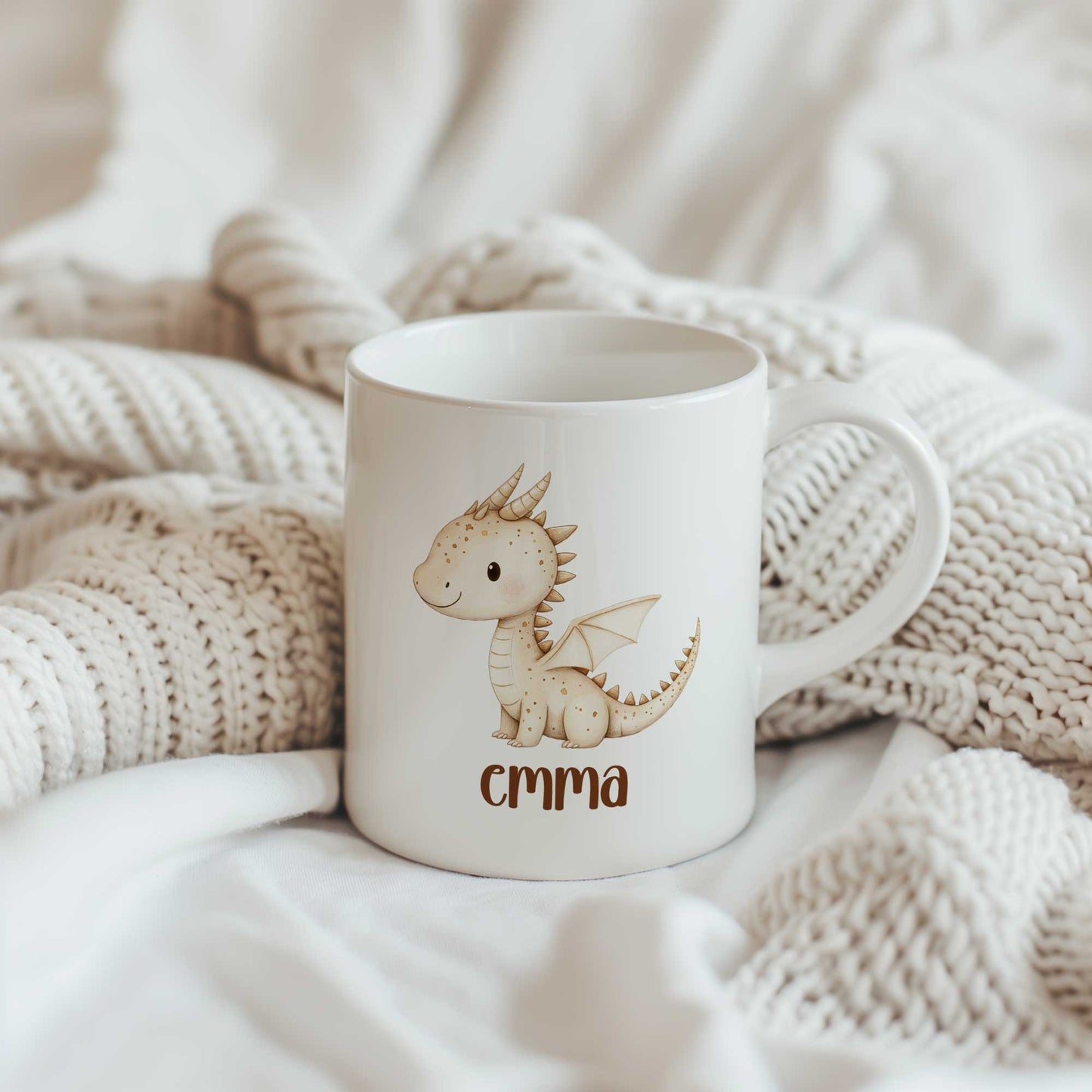 Witte mok met een schattig beige draakje en de naam Emma op een gebreide crème deken.
