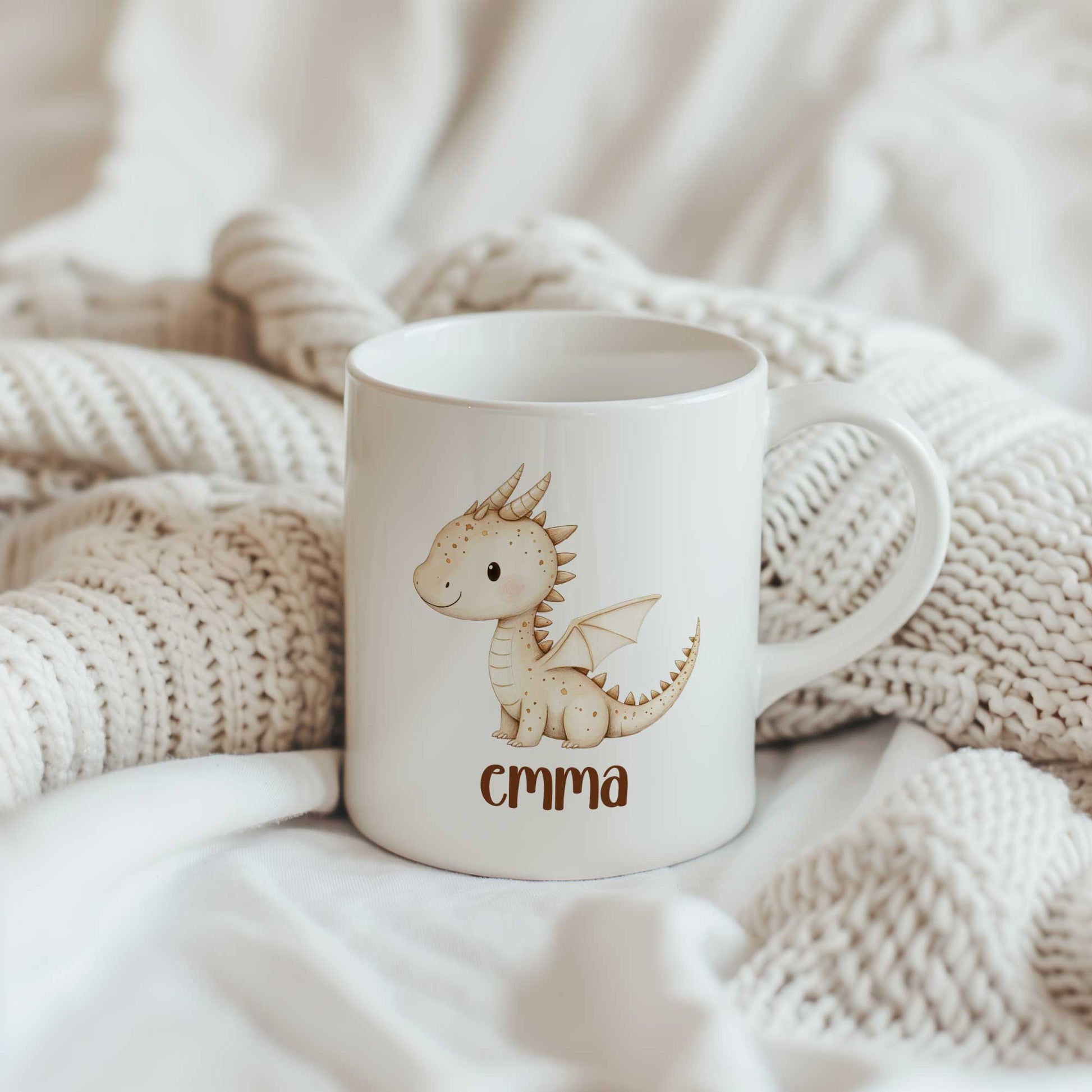 Witte mok met een schattig beige draakje en de naam Emma op een gebreide crème deken.