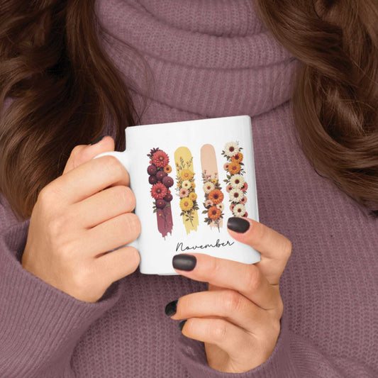 Vrouw in paarse trui houdt een mok vast met chrysanten in warme herfsttinten op gekleurde brushstrepen, met de tekst ‘November’.