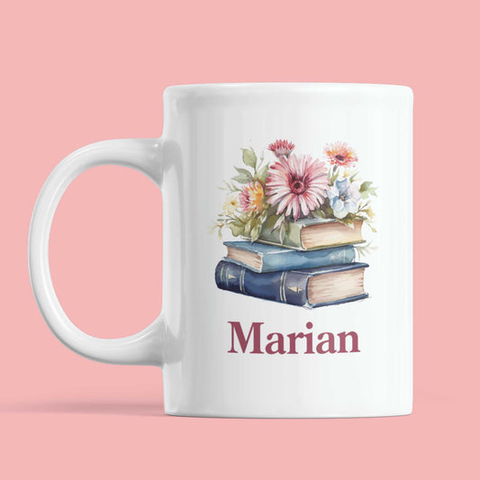 Witte mok met illustratie van drie boeken met bloemen en de naam "Marian", op een roze achtergrond