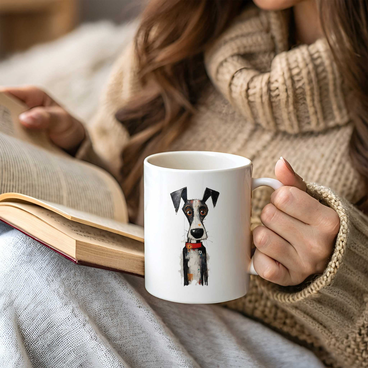 Vrouw in beige trui houdt een witte mok vast met een zwart-witte artistieke hond met grote oren, oranje ogen en rode halsband, terwijl een open boek op haar schoot ligt.