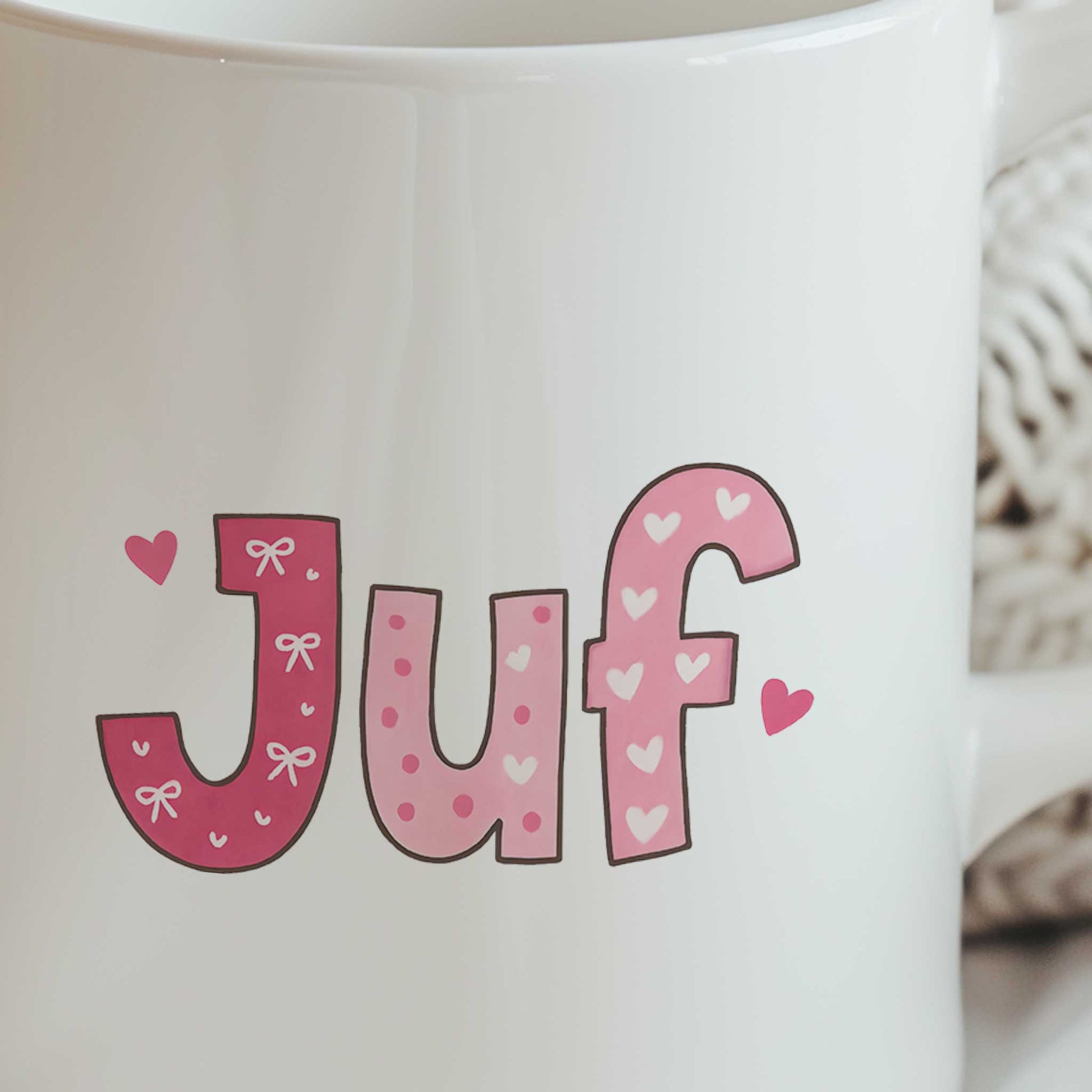Close-up van roze letters met strikjes en hartjes die samen de tekst Juf vormen op een witte mok