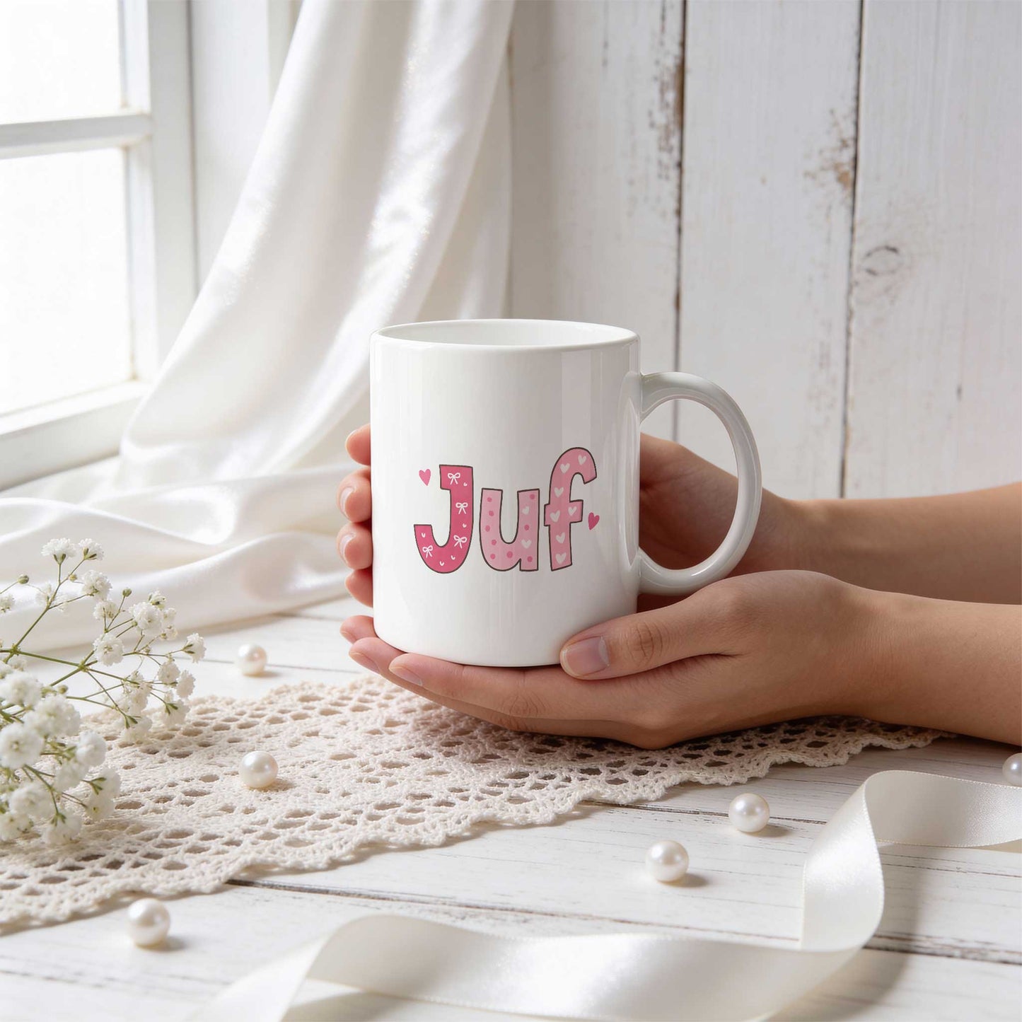 Sfeerfoto van een witte mok met roze letters, strikjes en hartjes die samen de tekst Juf vormen, vastgehouden in twee handen