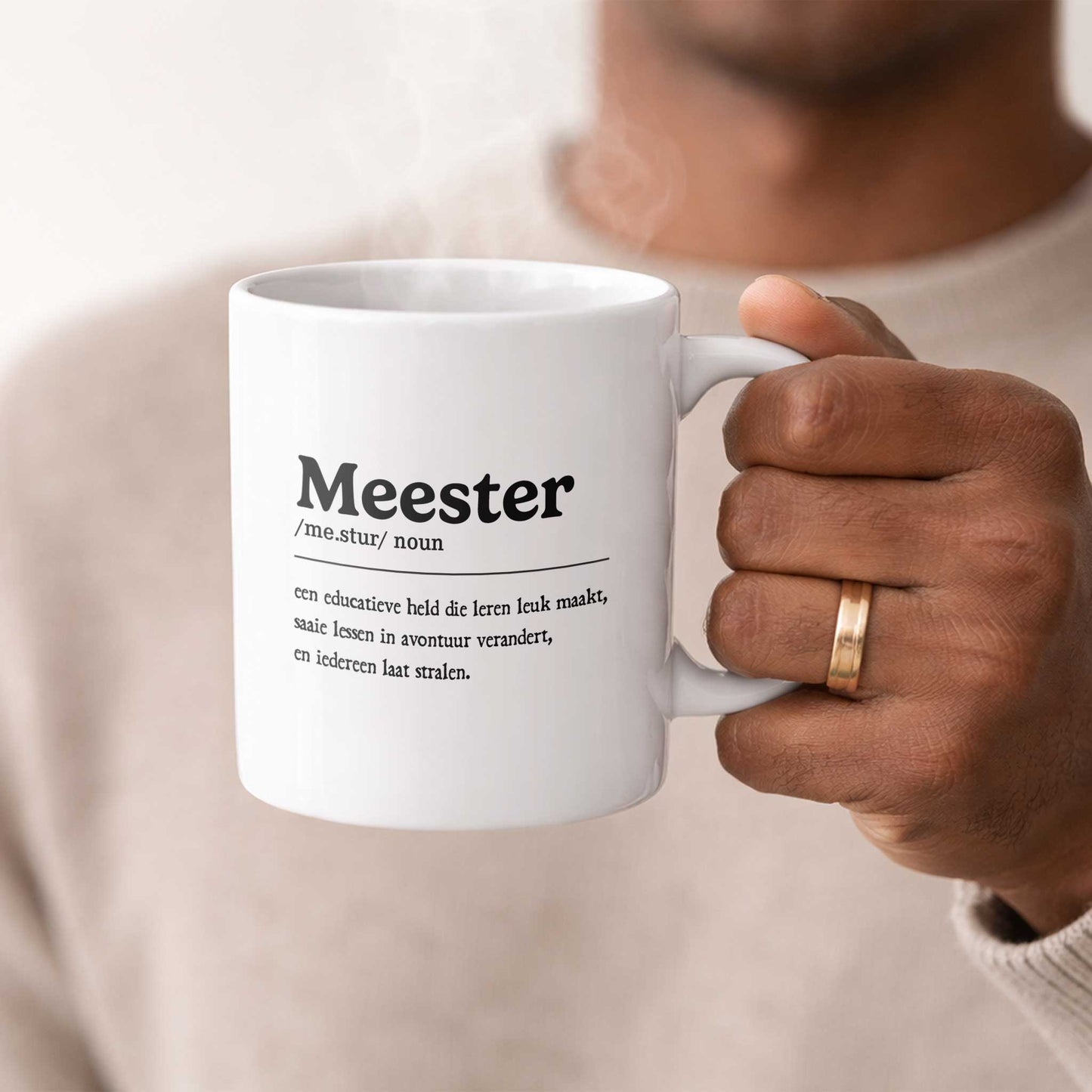 Sfeerfoto van een witte mok met de tekst "Meester", vastgehouden in een hand