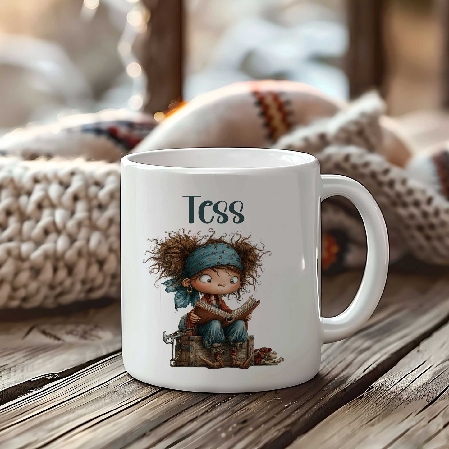 Witte mok op een houten tafel met de naam Tess boven een illustratie van een klein piratenkind dat op een houten kist zit en een boek leest.