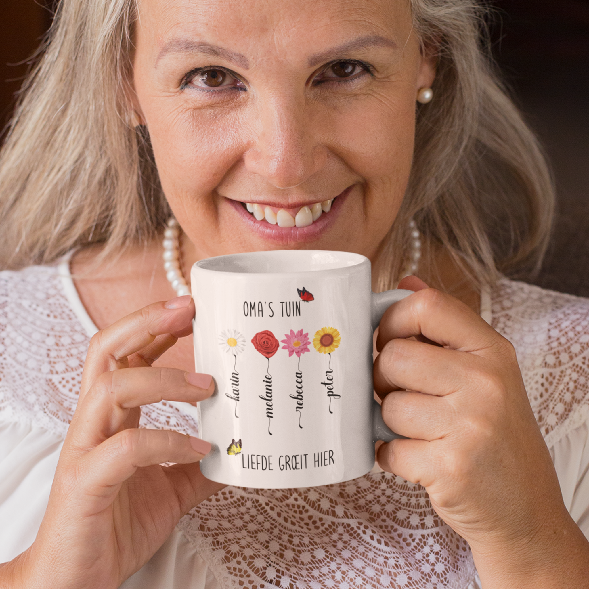een oudere vrouw met gepersonaliseerde mok voor oma met de tekst oma's tuin, liefde groet hier. Met verschillende bloemen en de namen van de kleinkinderen in de vorm van een bloemstengel .