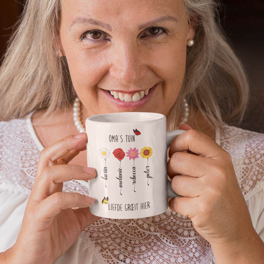 een oudere vrouw met gepersonaliseerde mok voor oma met de tekst oma's tuin, liefde groet hier. Met verschillende bloemen en de namen van de kleinkinderen in de vorm van een bloemstengel .