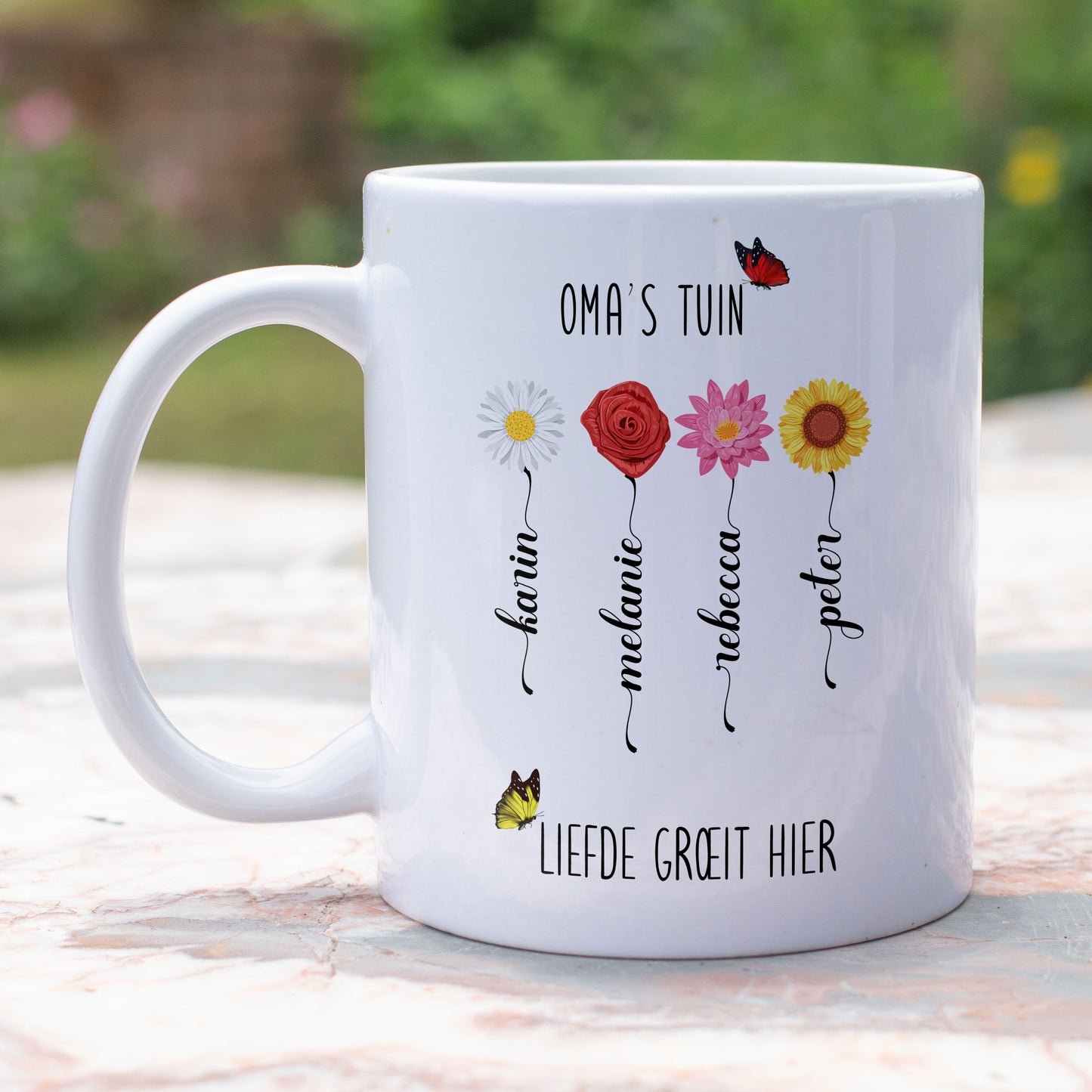 gepersonaliseerde mok voor oma met de tekst oma's tuin, liefde groet hier. Met verschillende bloemen en de namen van de kleinkinderen in de vorm van een bloemstengel buiten op een tuintafel