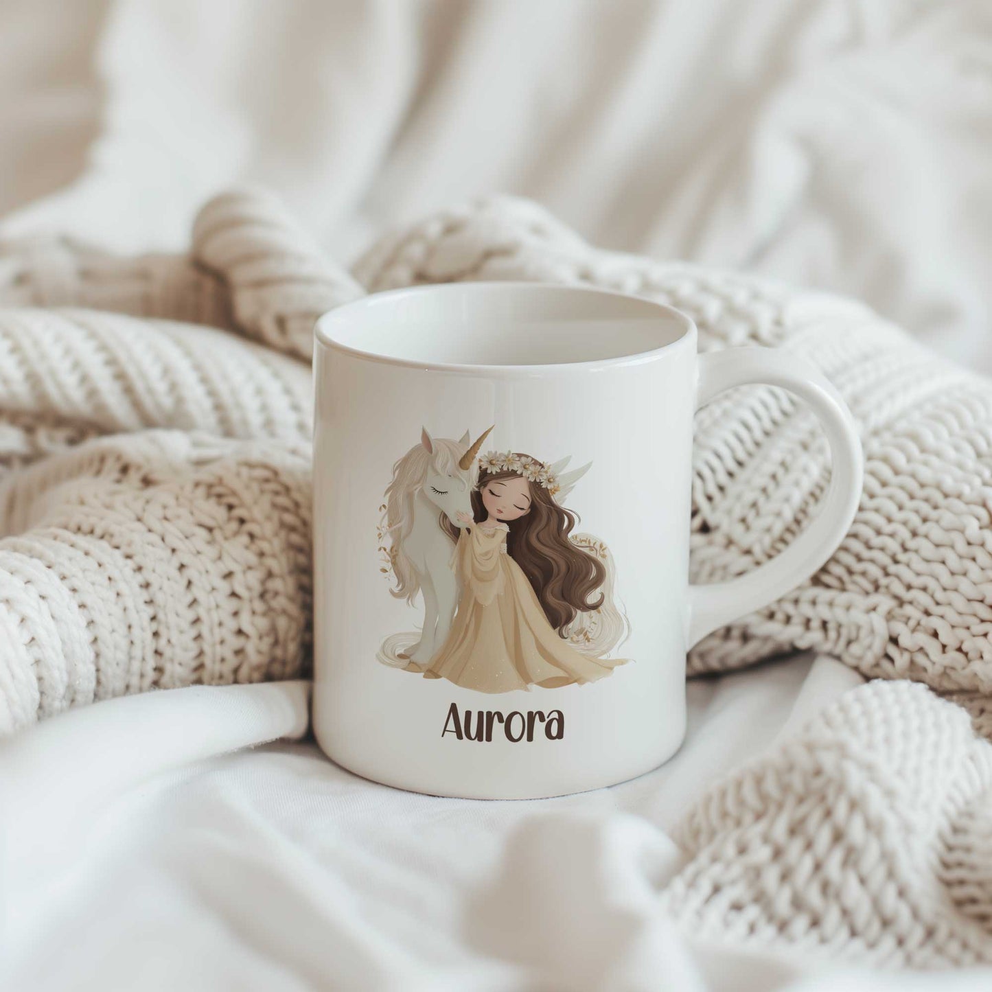 Witte mok met een prinses die een witte eenhoorn knuffelt. Onder de illustratie staat de naam Aurora. De mok staat tussen gebreide beige dekens.