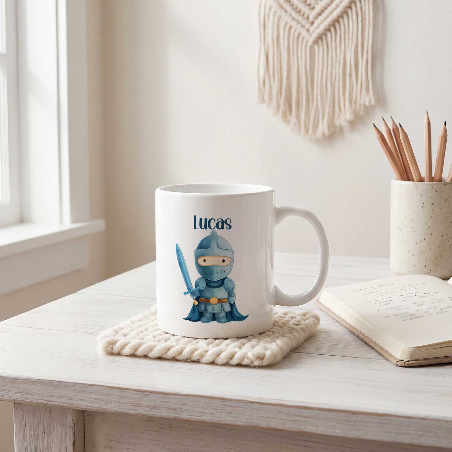 Witte mok met de naam Lucas en een illustratie van een blauwe ridder met een zwaard op een houten bureau naast een notitieboek en een pot met potloden.
