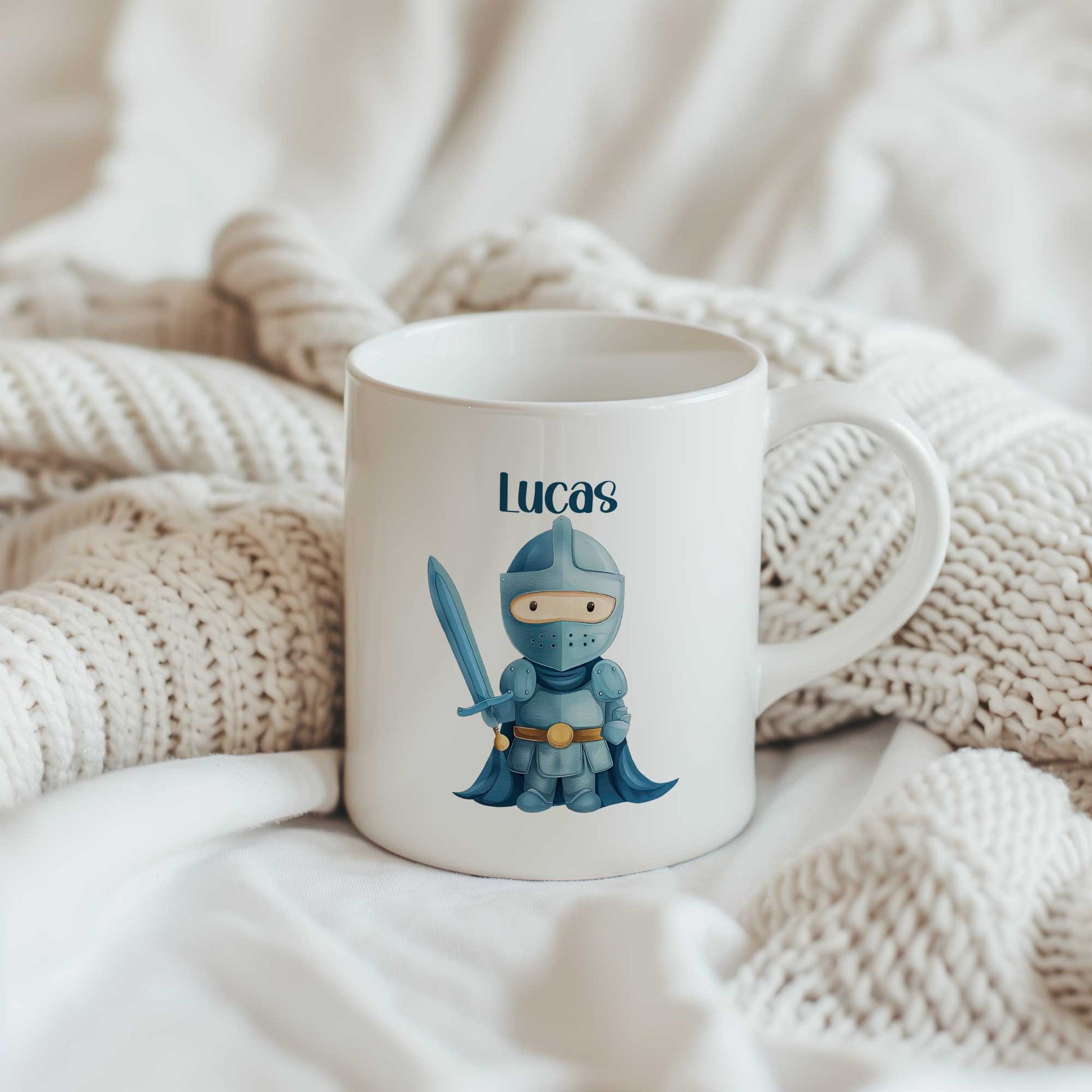 Witte mok met de naam Lucas en een illustratie van een blauwe ridder met een zwaard tussen gebreide beige dekens.