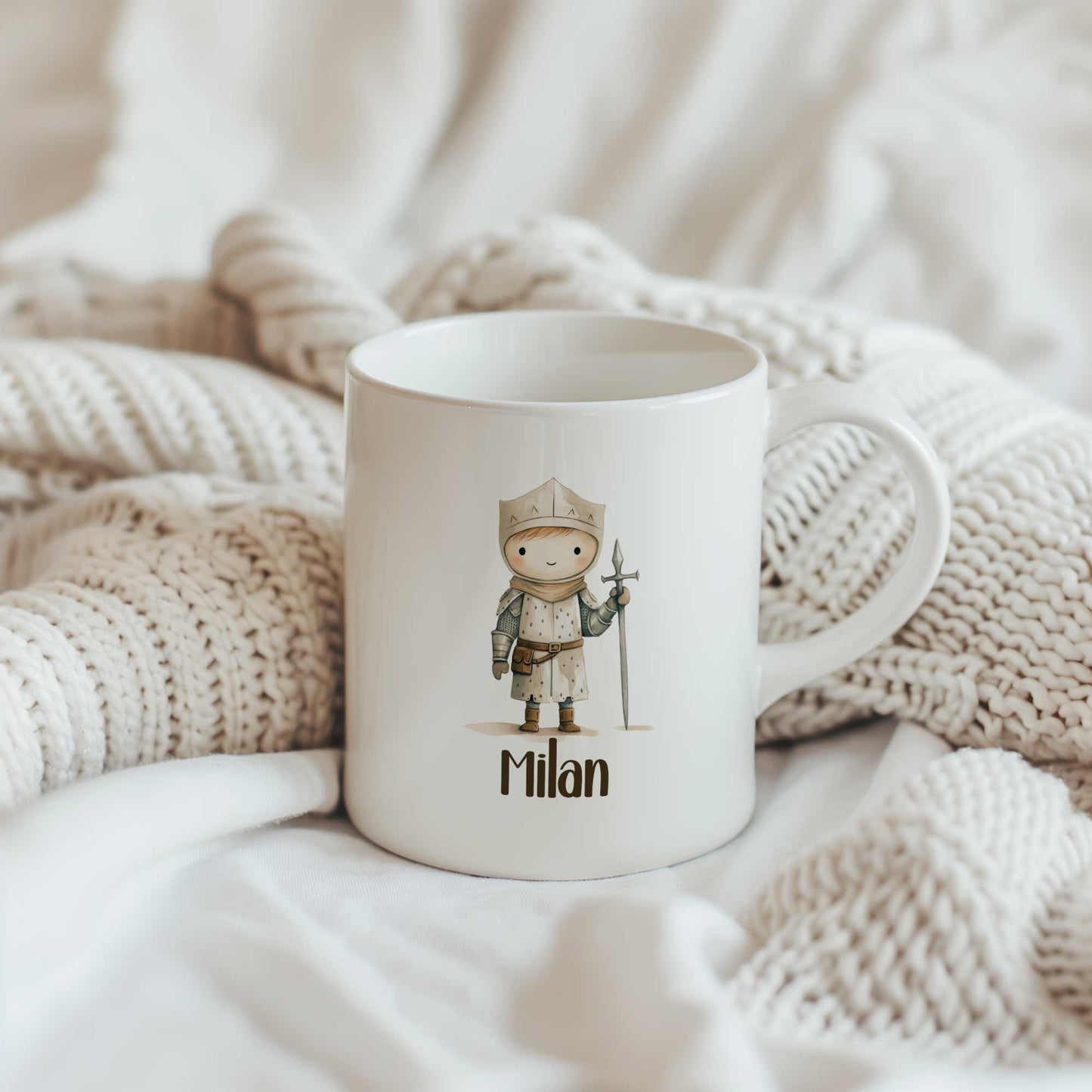 Witte mok met een illustratie van een kleine ridder en de naam Milan tussen gebreide beige dekens.