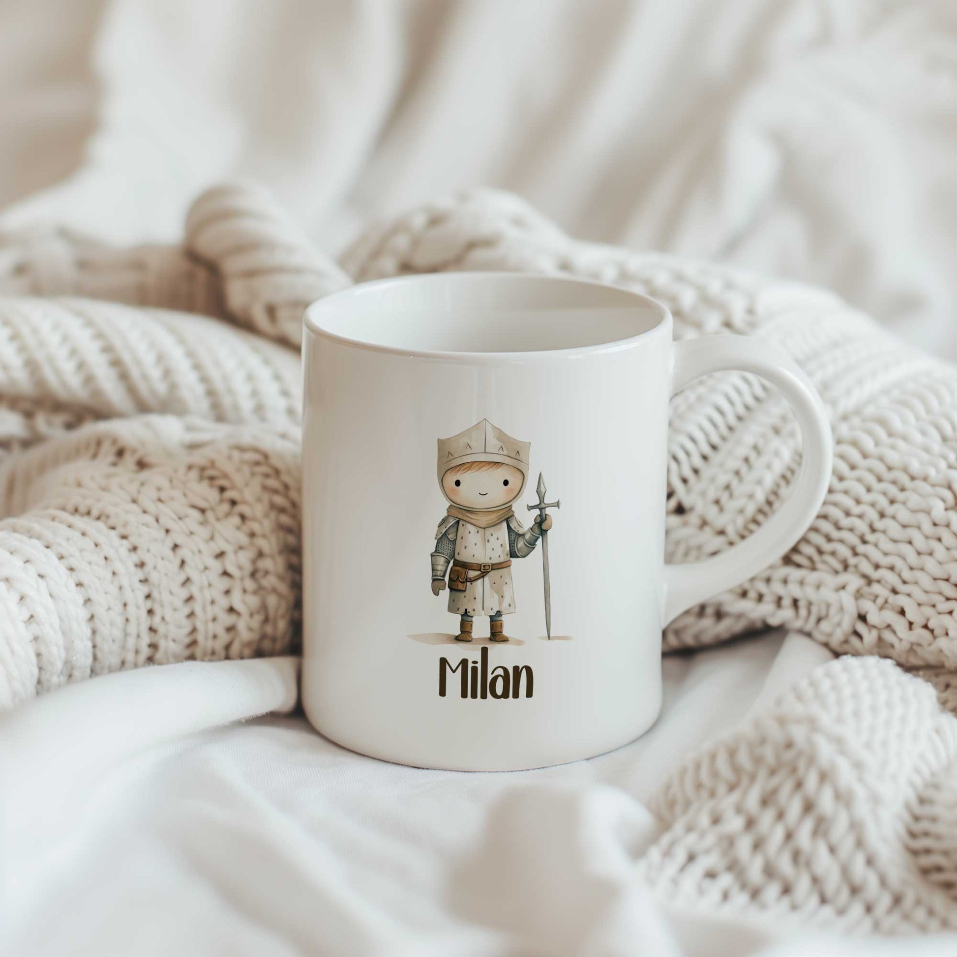 Witte mok met een illustratie van een kleine ridder en de naam Milan tussen gebreide beige dekens.