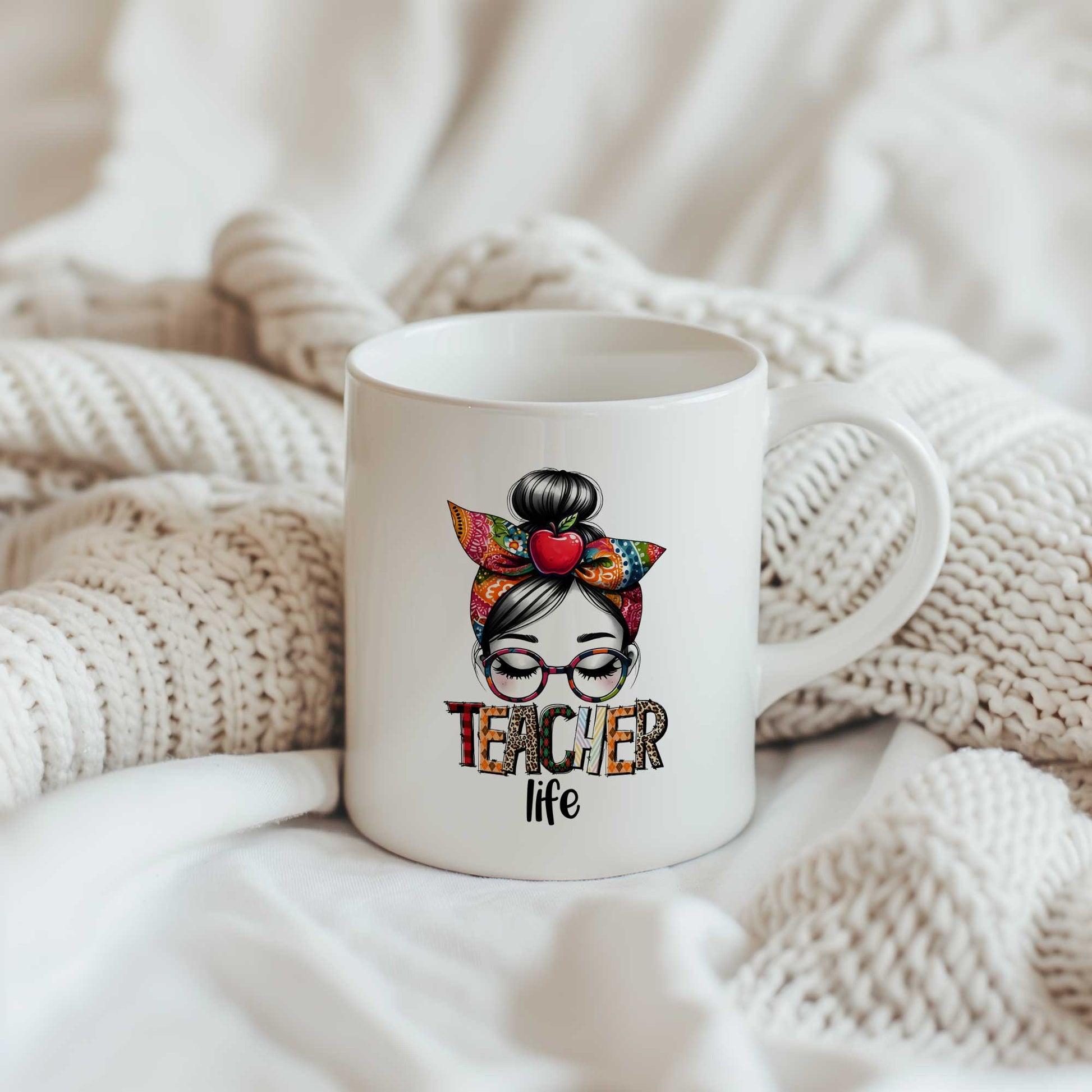 Witte keramische mok met illustratie van een vrouw met bril, kleurrijke strik en de tekst "Teacher Life", geplaatst op een zachte beige gebreide deken.
