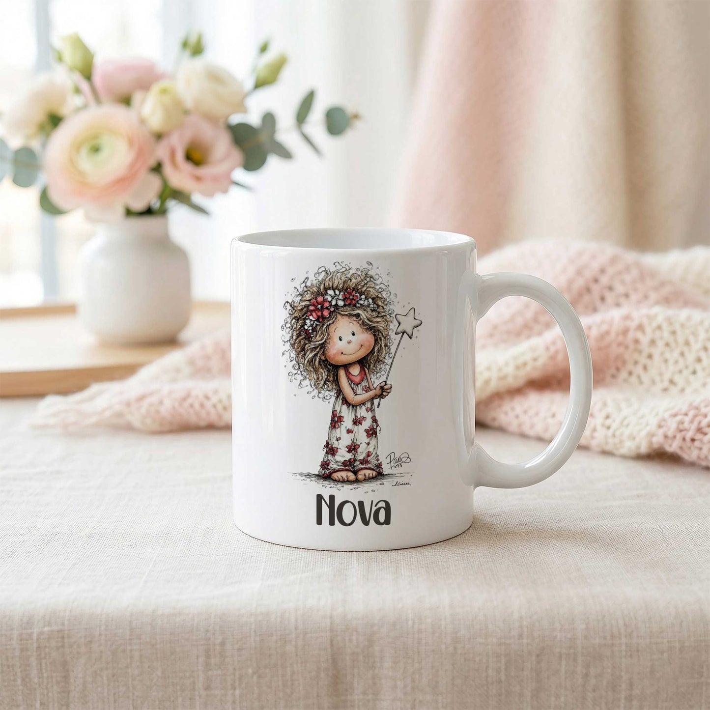 Witte mok met fee-illustratie en naam Nova op een lichte tafel naast een zachtroze gebreide deken en een vaas met bloemen.