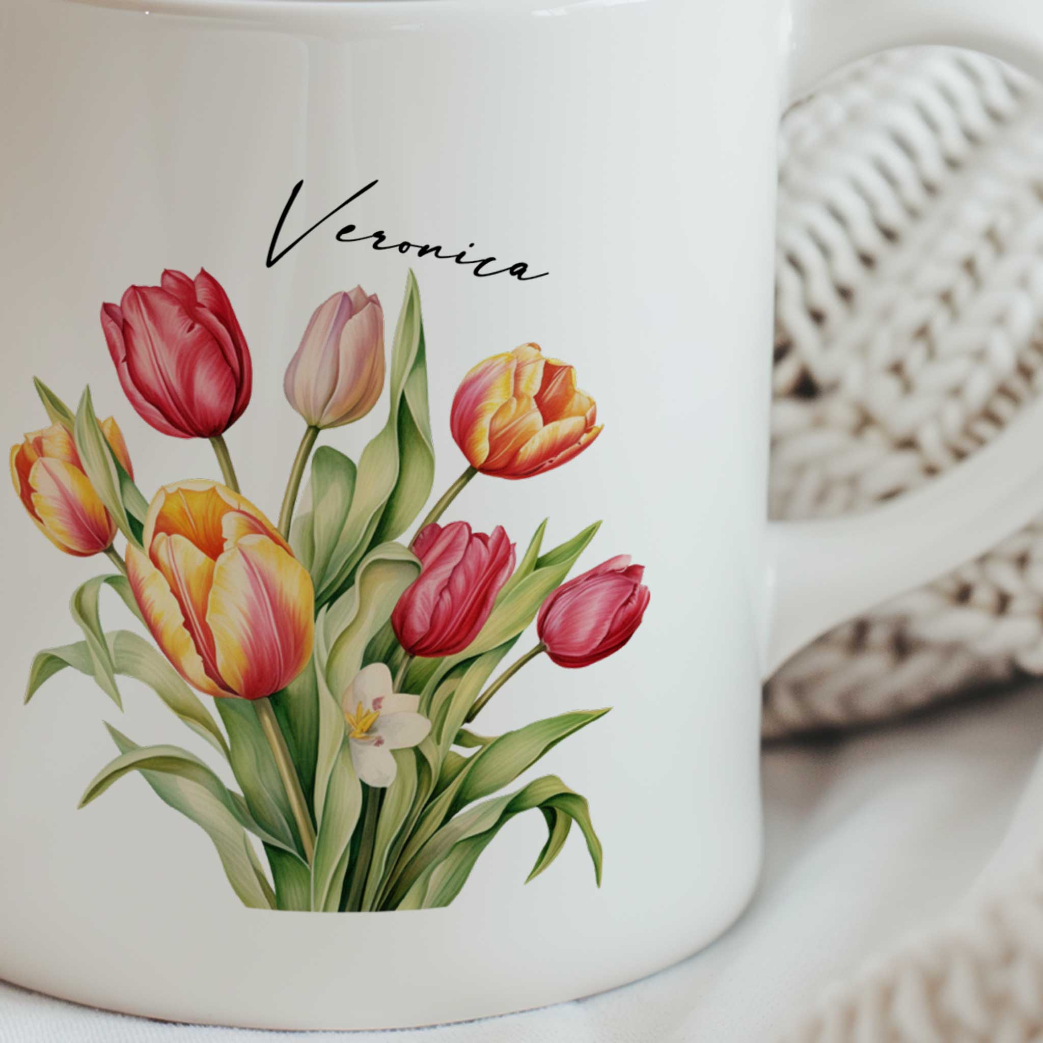 Close-up van een witte mok met een kleurrijk boeket tulpen in rood, roze, geel en oranje tinten en een gepersonaliseerde naam boven het boeket.