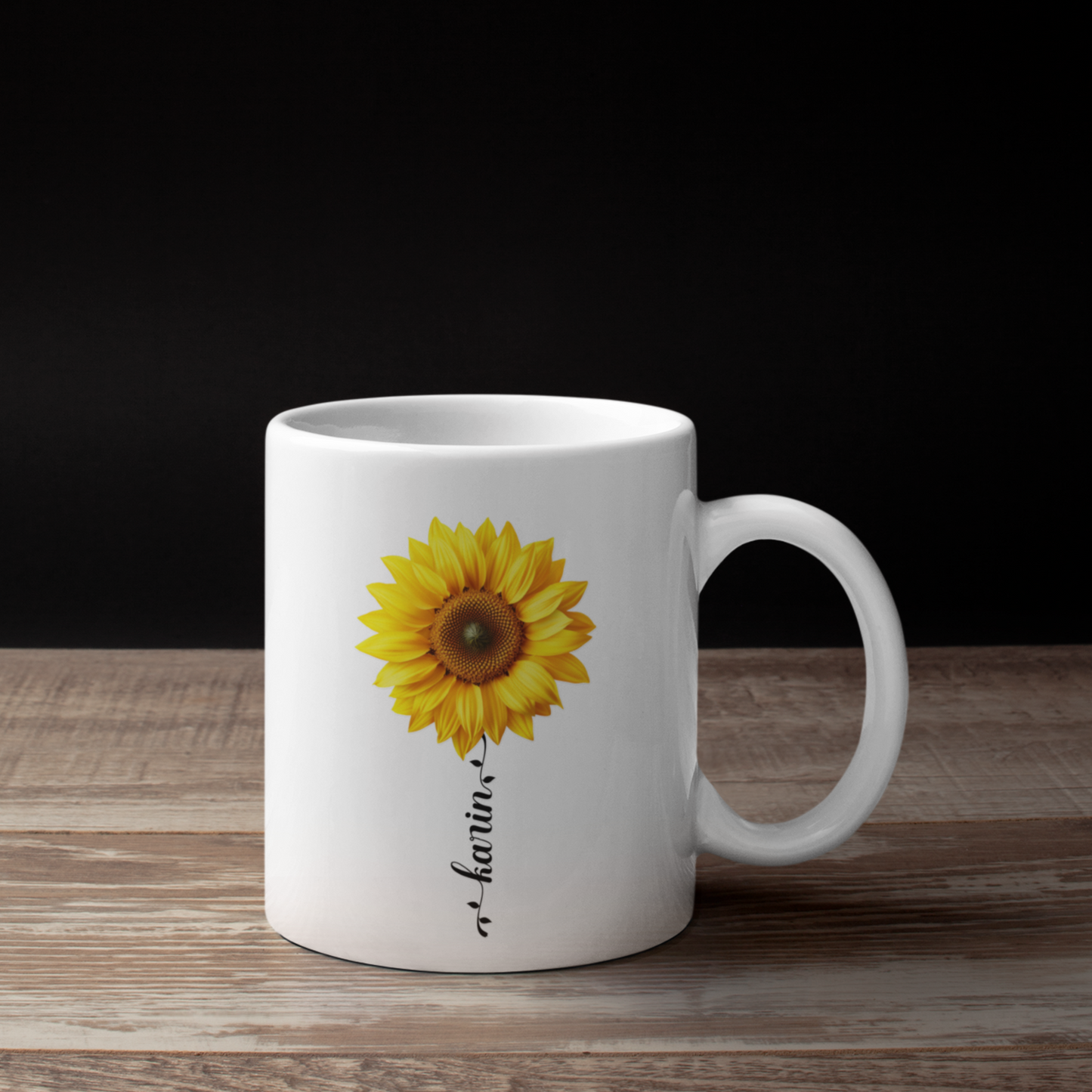 witte mok met zonnebloem en aanpasbare naam in een zwart sierlijke lettertype in de vorm van een bloemstengel op een houten tafel