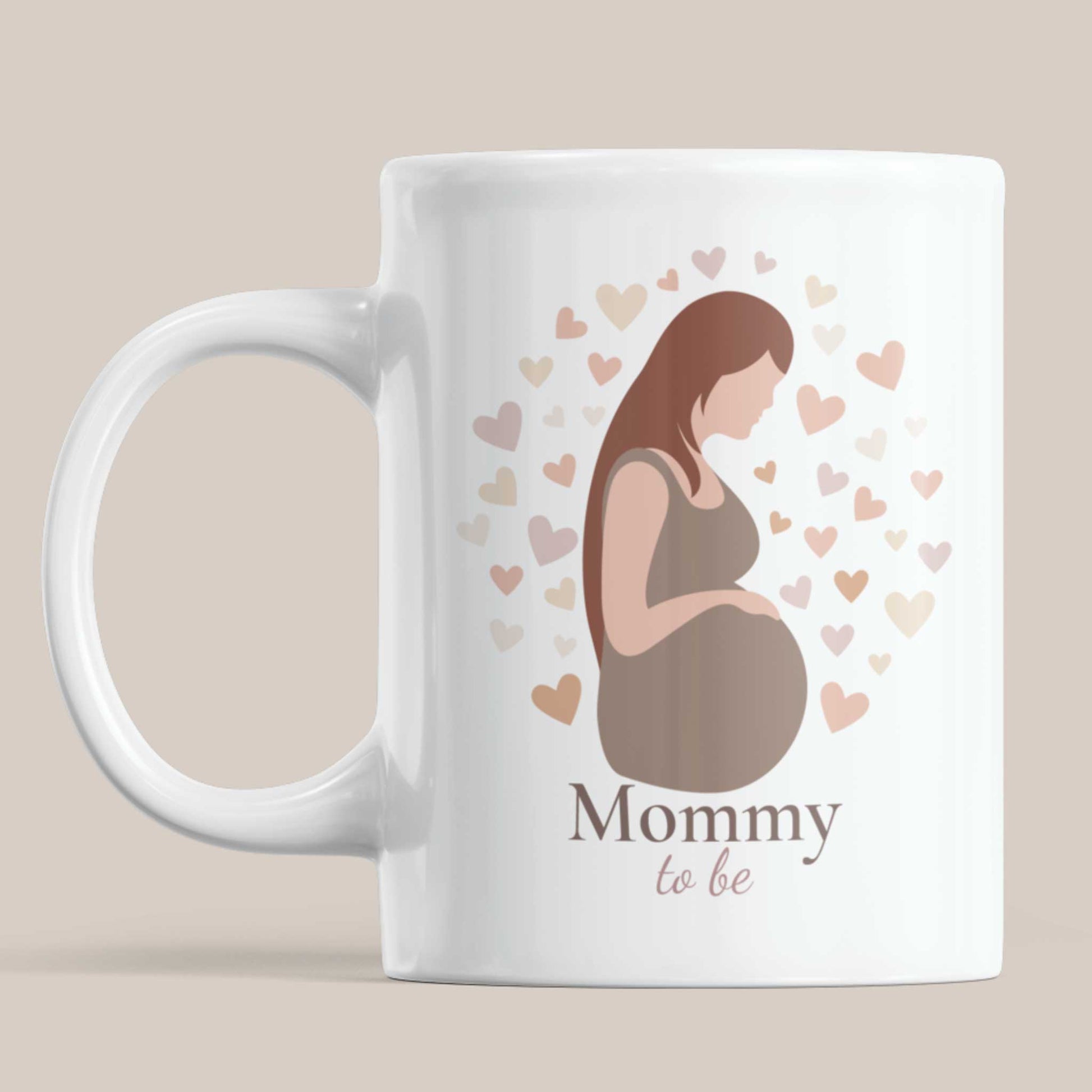 Witte keramische Mommy To Be mok op beige achtergrond met minimalistische illustratie van zwangere vrouw en pastel hartjes.