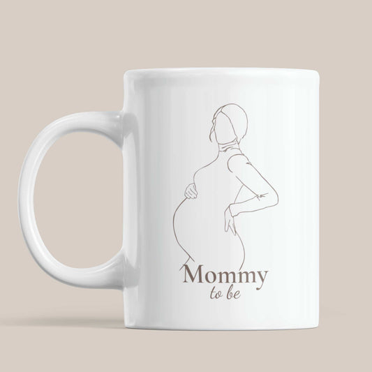 Minimalistische witte mok met lijnillustratie van een zwangere vrouw en de tekst Mommy to be op een beige achtergrond