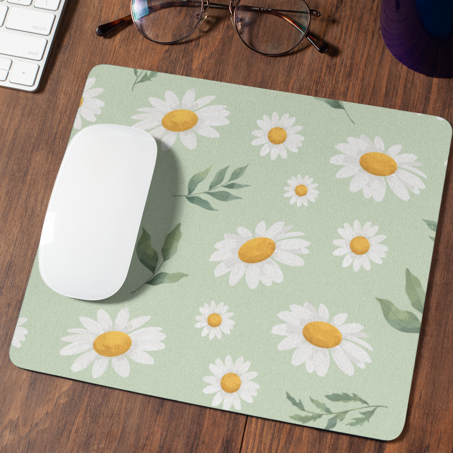 muismat met een bloemenpatroon, Margrietjes en blaadjes op een licht groene ondergrond op een donkerhouten bureau met een witte muis en een leesbril