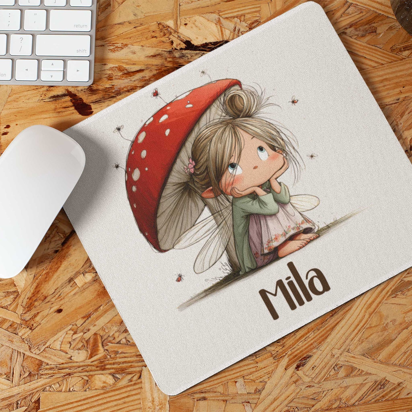 Muismat op een houten bureau met een illustratie van een fee onder een rode paddenstoel en de naam Mia.