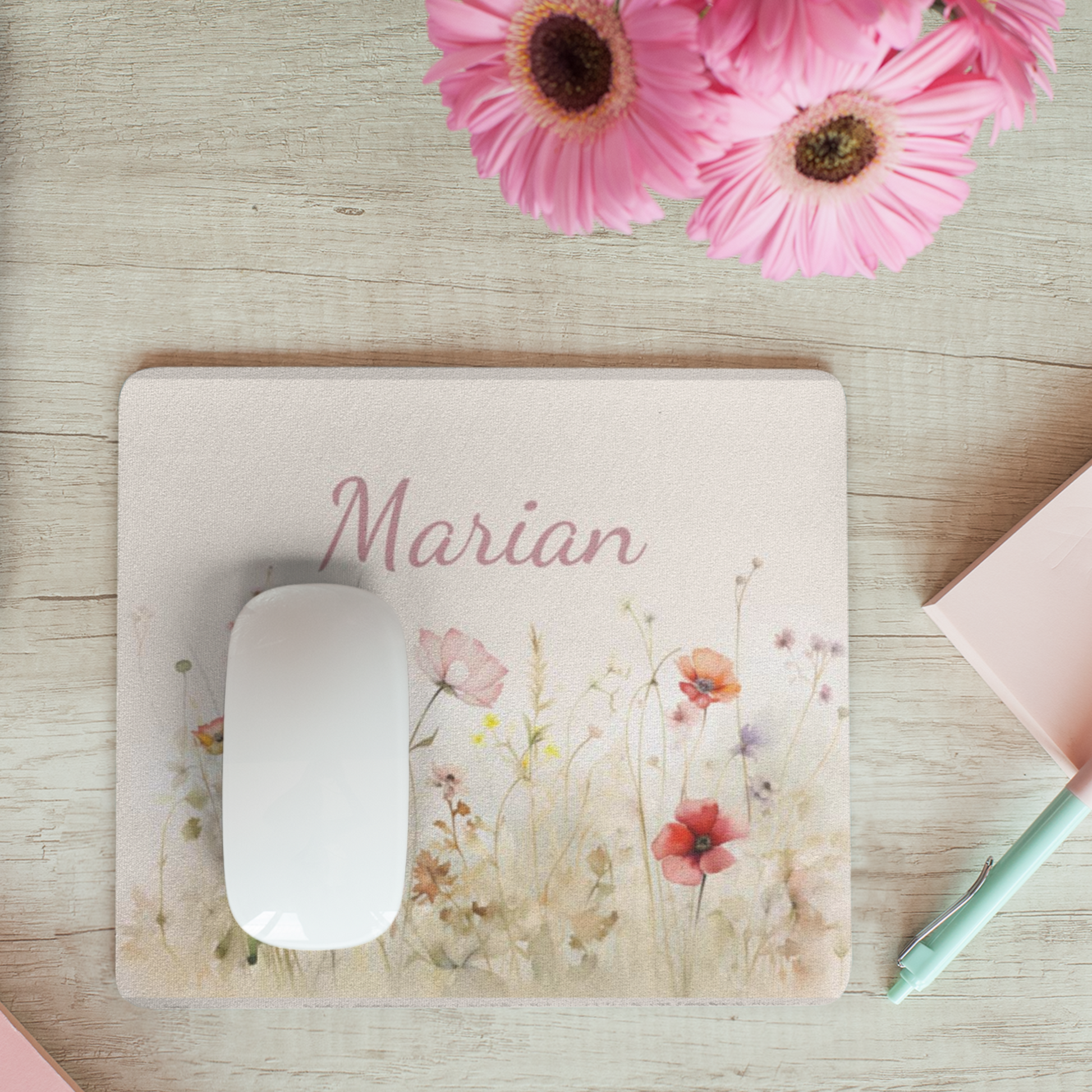 muismat met wilde bloemen tegen een zacht creme achtergrond met  een naam in zachtroze. Naam is aanpasbaar. Muismat ligt op een licht houten bureau met roze bloemen erbij.