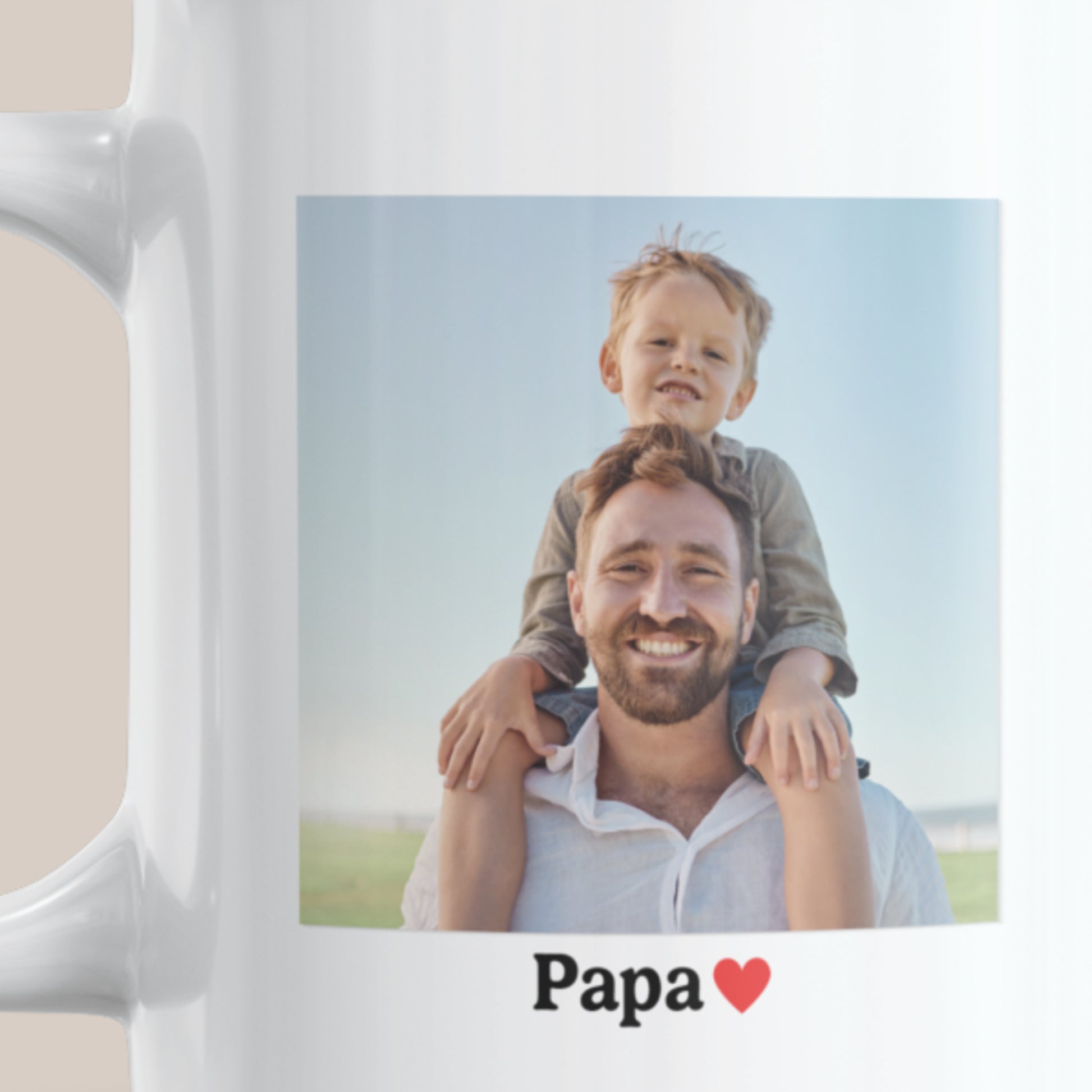 Detailfoto van een witte keramische mok met een vierkante foto van een vader met kind op zijn schouders en daaronder de tekst “Papa” met een rood hartje.