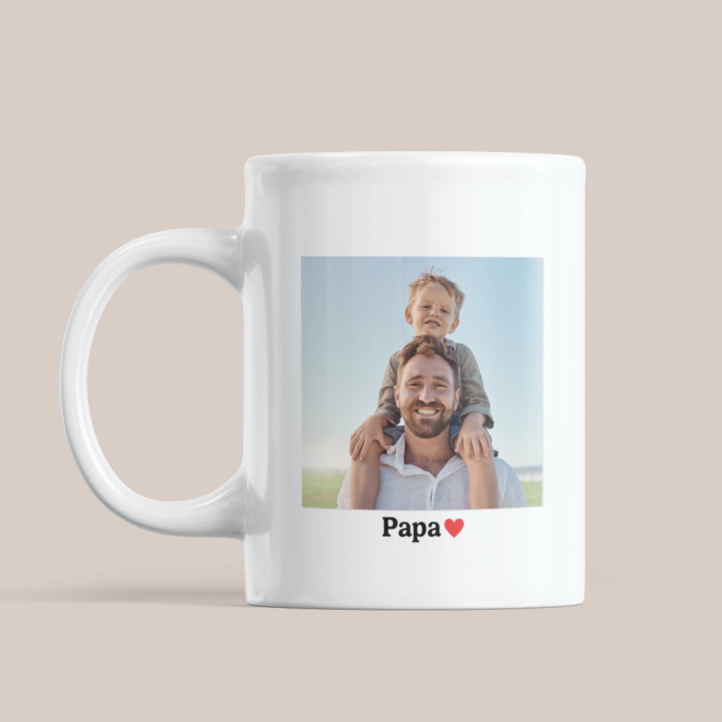 Witte keramische mok op een beige achtergrond met een foto van een vader met kind op zijn schouders en daaronder de tekst “Papa” met een rood hartje.
