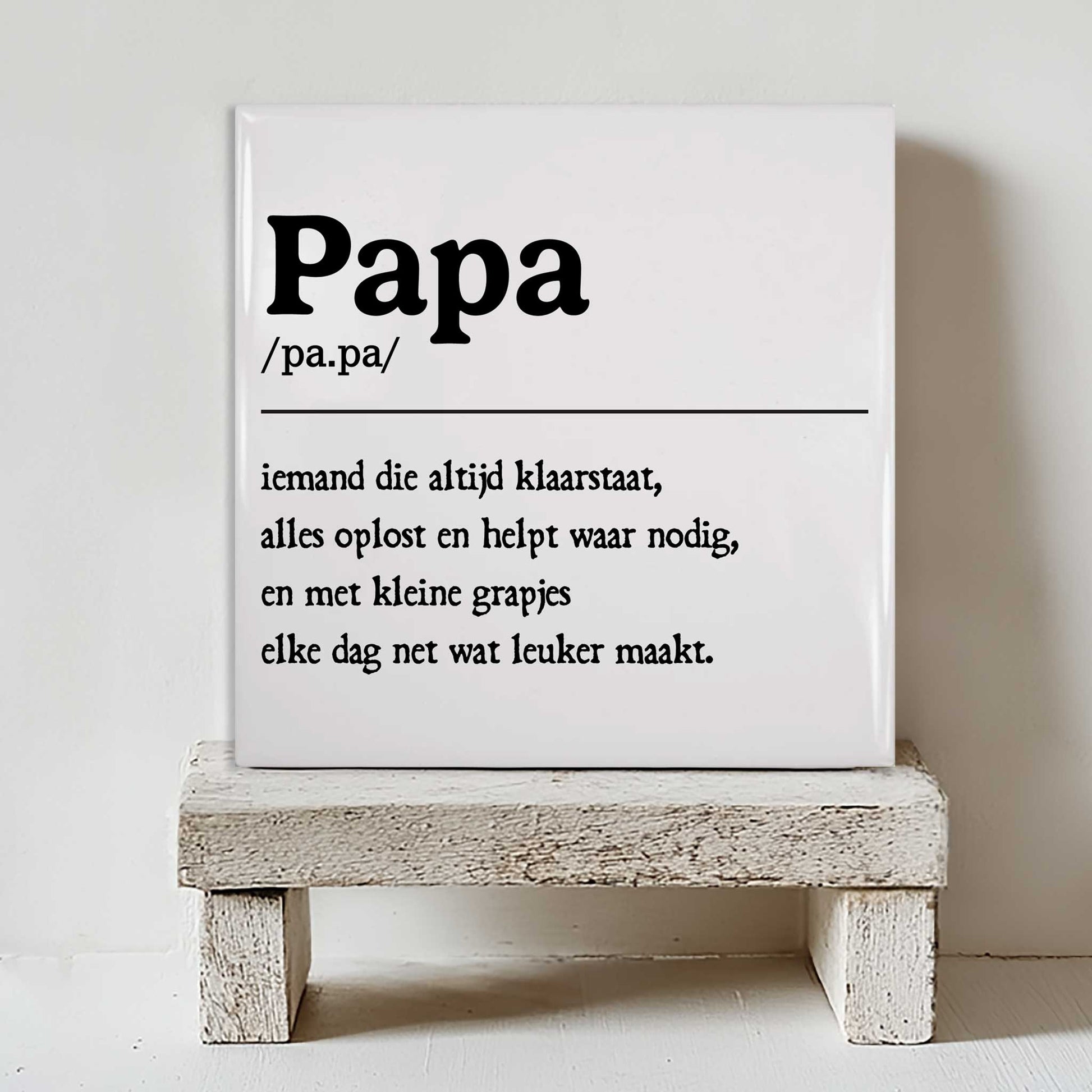 Minimalistisch keramisch papa tegeltje met zwarte typografie geplaatst op een klein wit houten krukje tegen een lichte muur