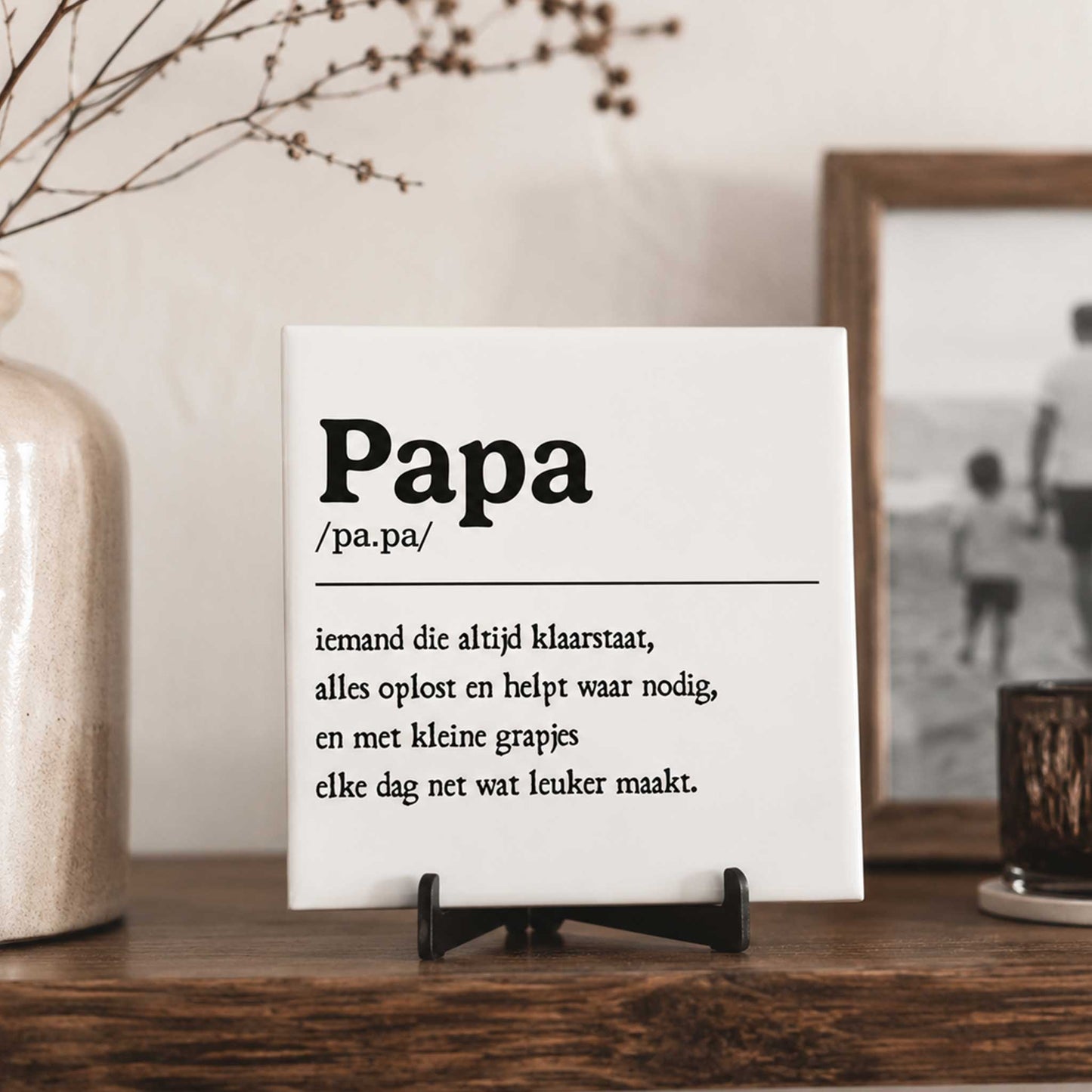 Wit keramisch tegeltje met de tekst “Papa” en een liefdevolle omschrijving geplaatst op een houten tafel naast een fotolijst en decoratie