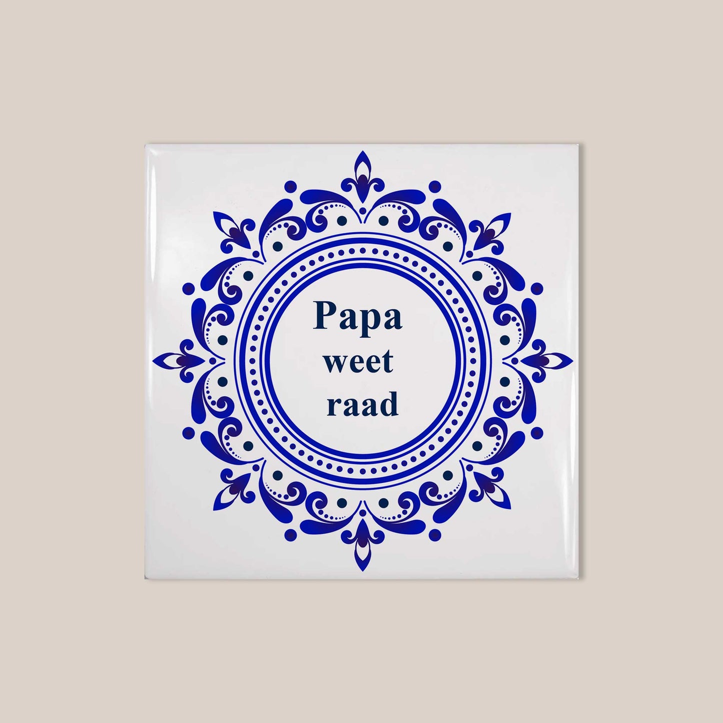Vierkant wit keramisch tegeltje met sierlijk blauw Delfts blauw ornament en de tekst “Papa weet raad” op beige achtergrond