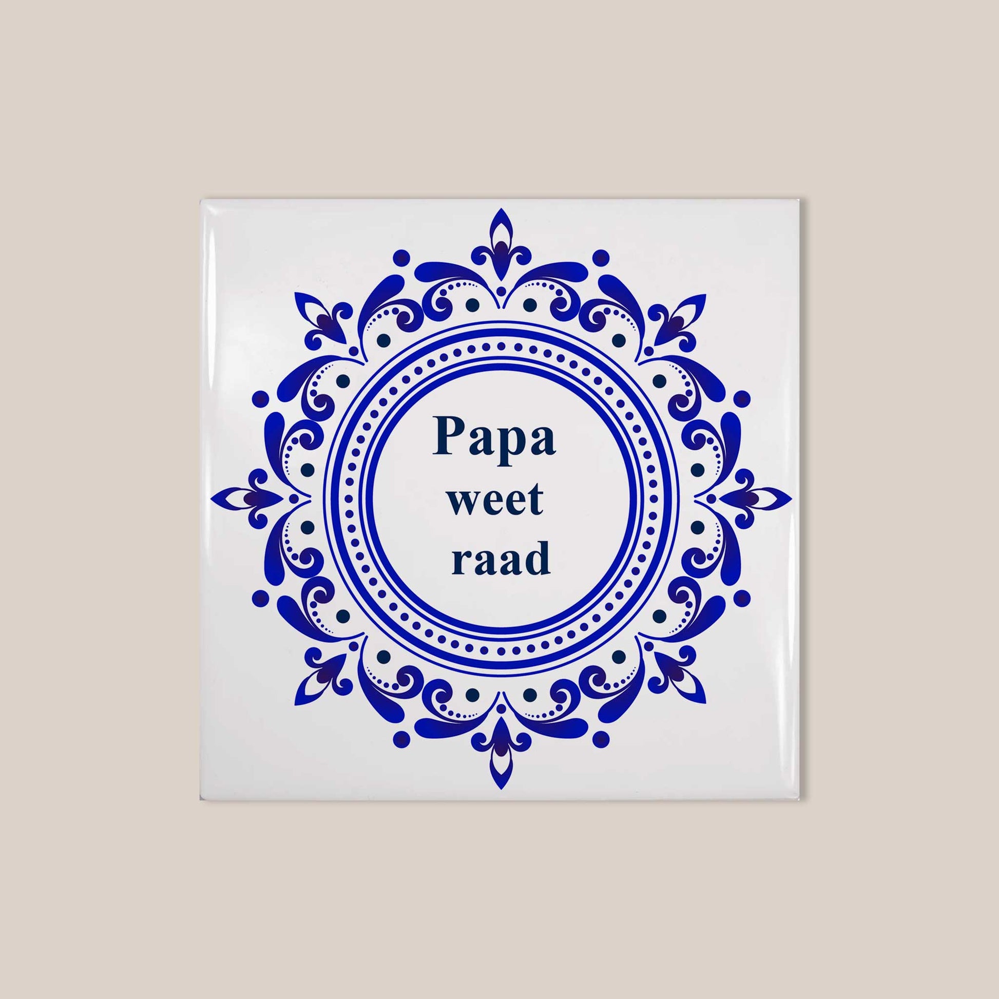 Vierkant wit keramisch tegeltje met sierlijk blauw Delfts blauw ornament en de tekst “Papa weet raad” op beige achtergrond