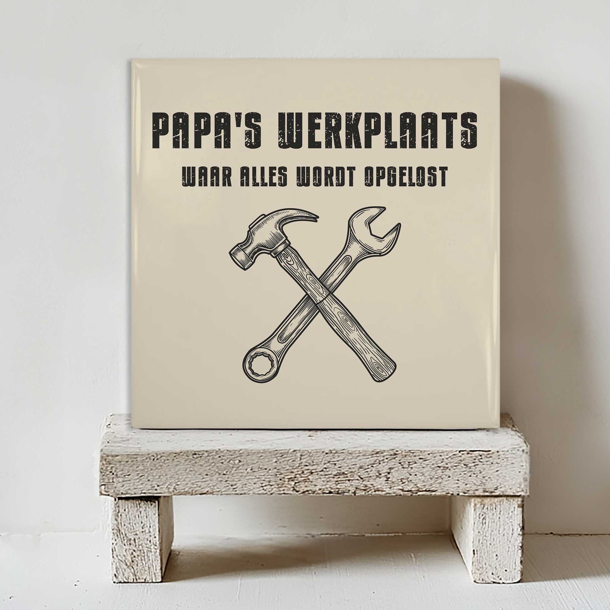 Stoer keramisch decoratietegeltje met hamer en steeksleutel illustratie geplaatst op een houten krukje tegen een lichte muur